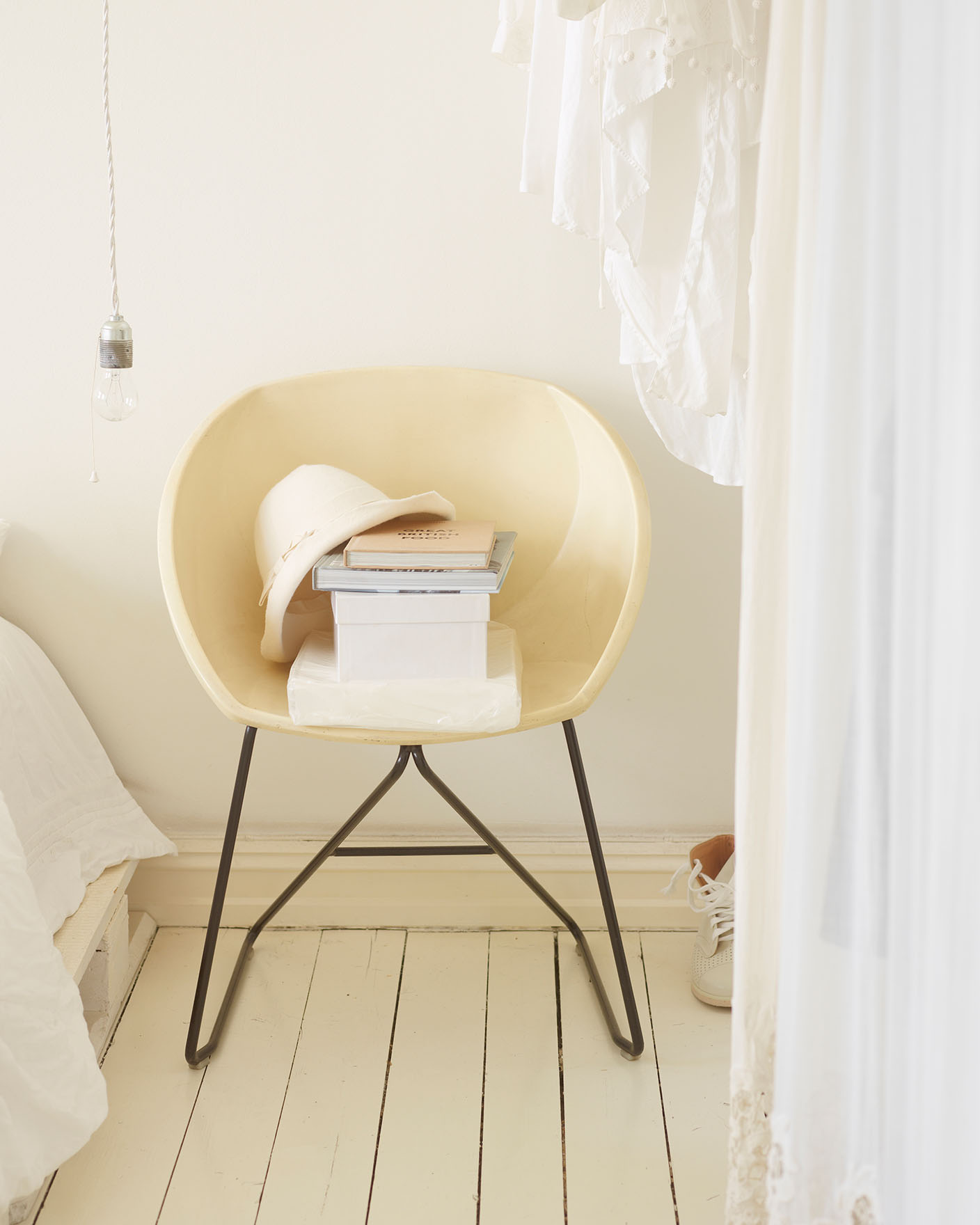 Krämfärgad stol med en hög böcker och en hatt, omgiven av mjuka vita textilier i ett ljust och luftigt rum, målat med Jotun 1624 Lätthet.