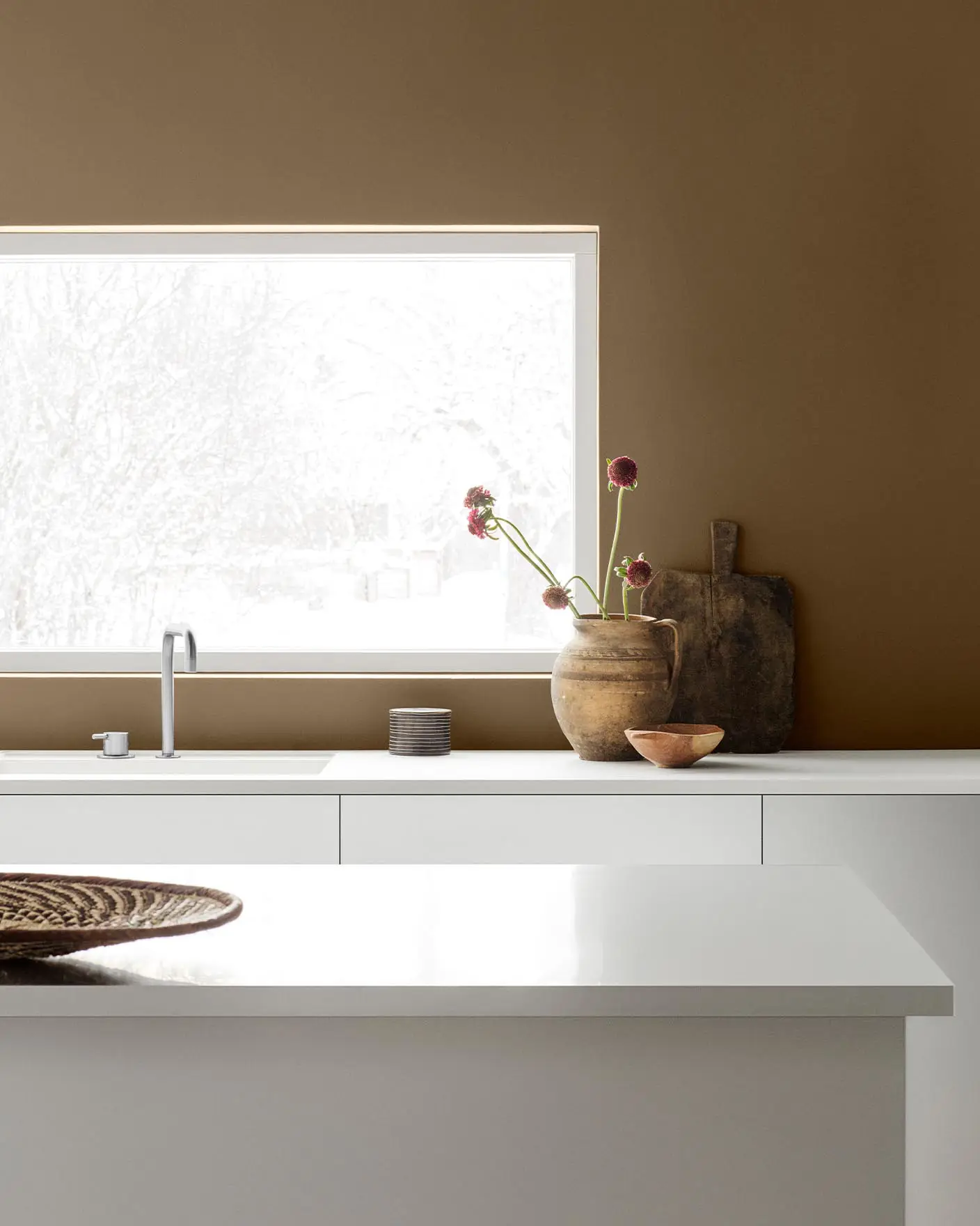 Minimalistisk kjøkken med hvite skap og innredning mot en gyldenbrun vegg malt med Jotun-fargen 10963 Golden Bronze.