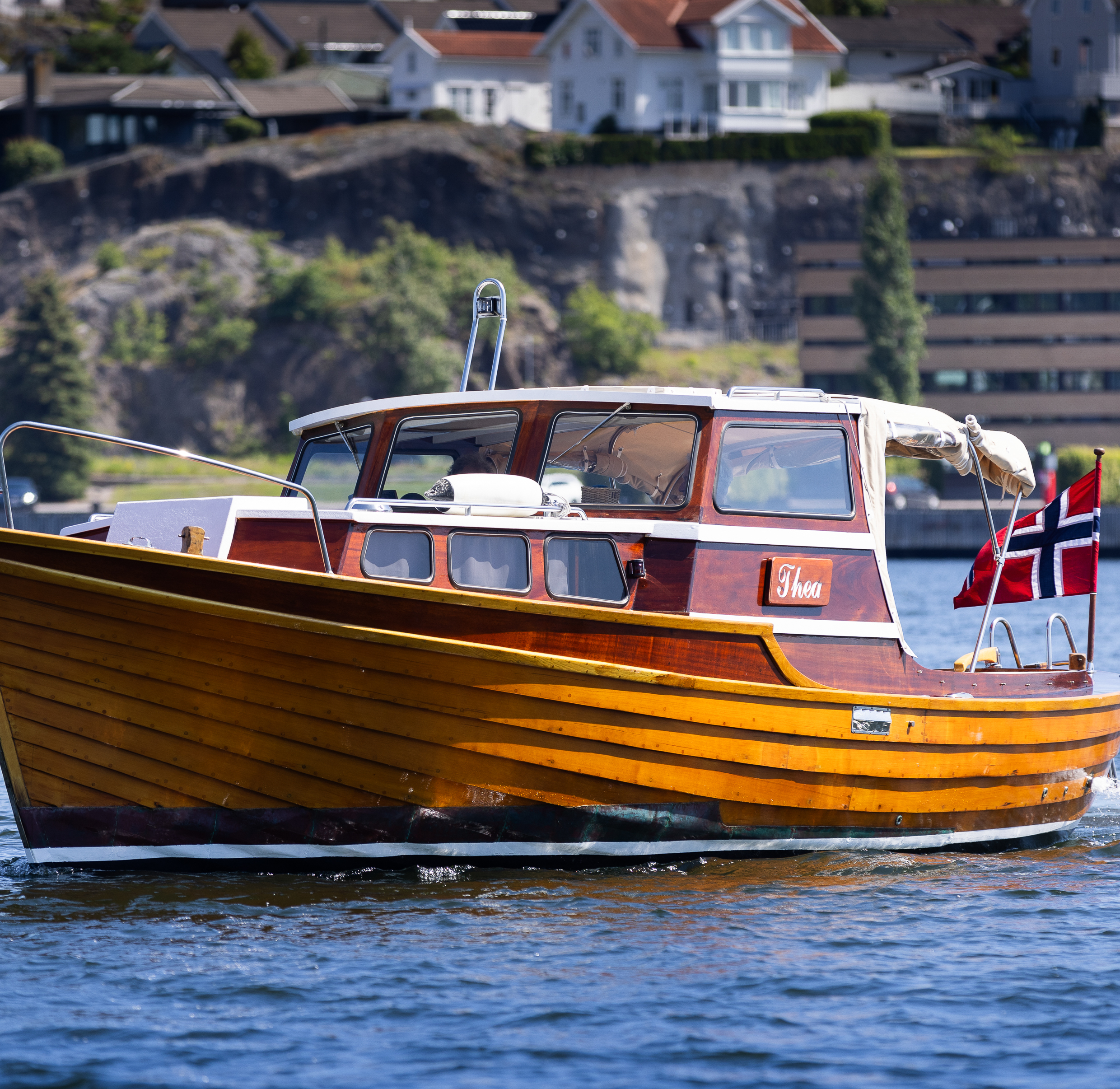 Blank og nypusset trebåt med norsk flagg, ute på fjorden en solrik sommerdag
