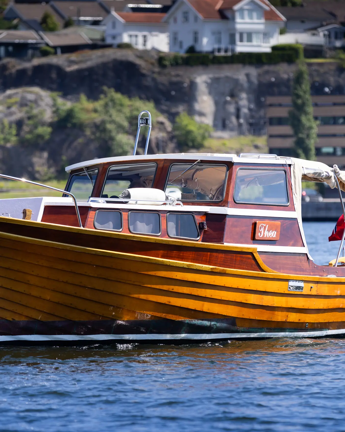 Blank og nypusset trebåt med norsk flagg, ute på fjorden en solrik sommerdag