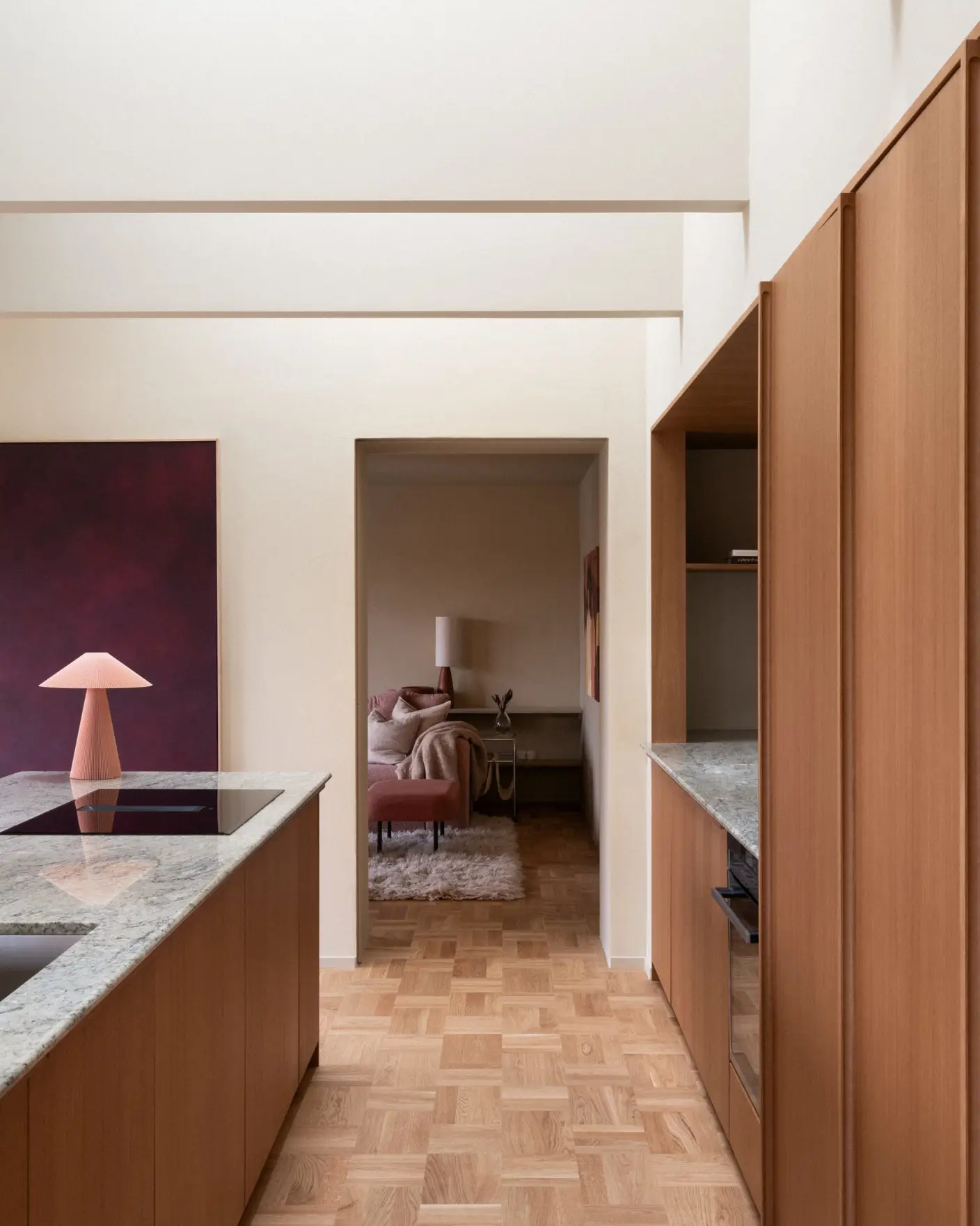 Moderne interiør i kjøkken med tregulv, elegante benkeplater i marmor og minimalistisk innredning. I bakgrunnen vises en koselig stue med designlampen som skaper lun stemning, Vegger og tak malt i gulbeige med Jotun 11173 Humble Yellow