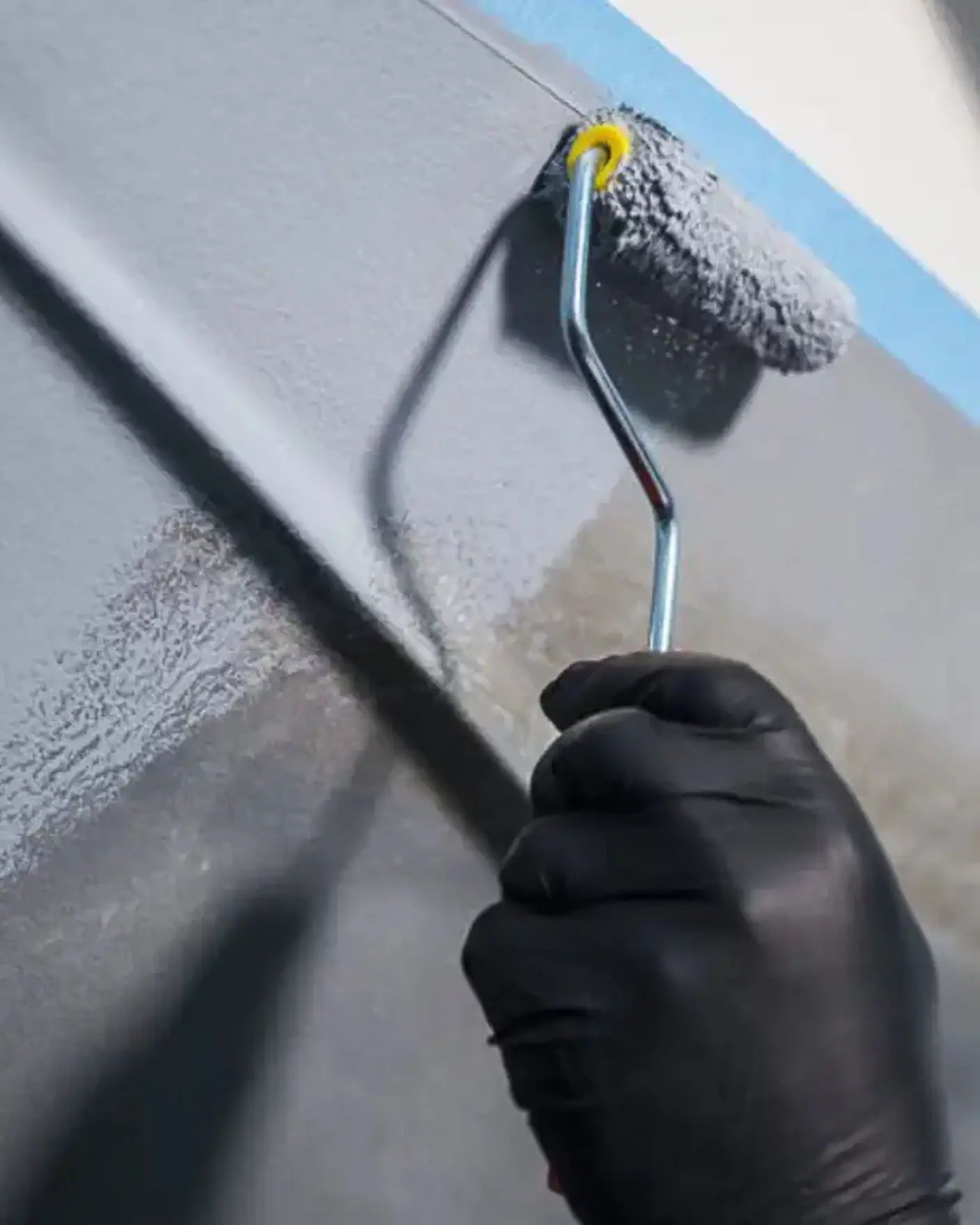 Hånd med sort hanske holder malingsrulle og påfører grunning av båt med produkter fra Jotun