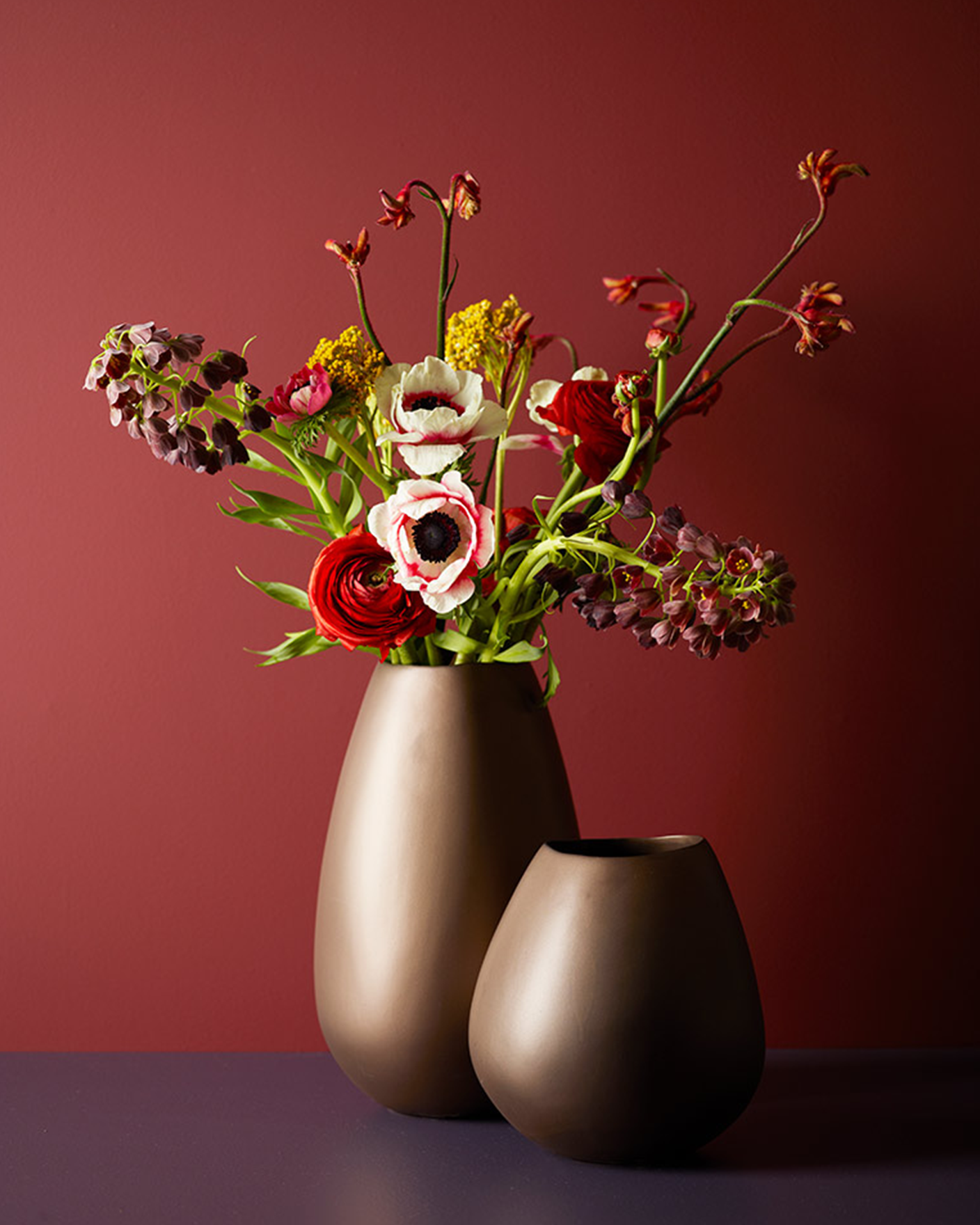 Elegant blomsteroppsats med røde, hvite og lilla blomster i en høy og lav brun vase på burgunder bakgrunn malt i Jotun 2846 Bordeaux.