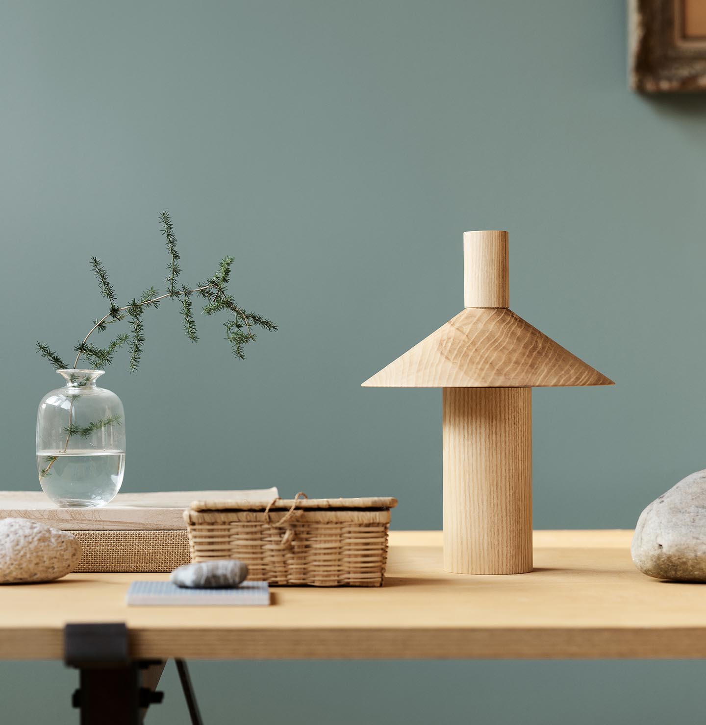 Minimalist decor with vase, books, and sculpture on a wooden table against a muted, bluish green background in the colour Jotun 6379 Cityscape.