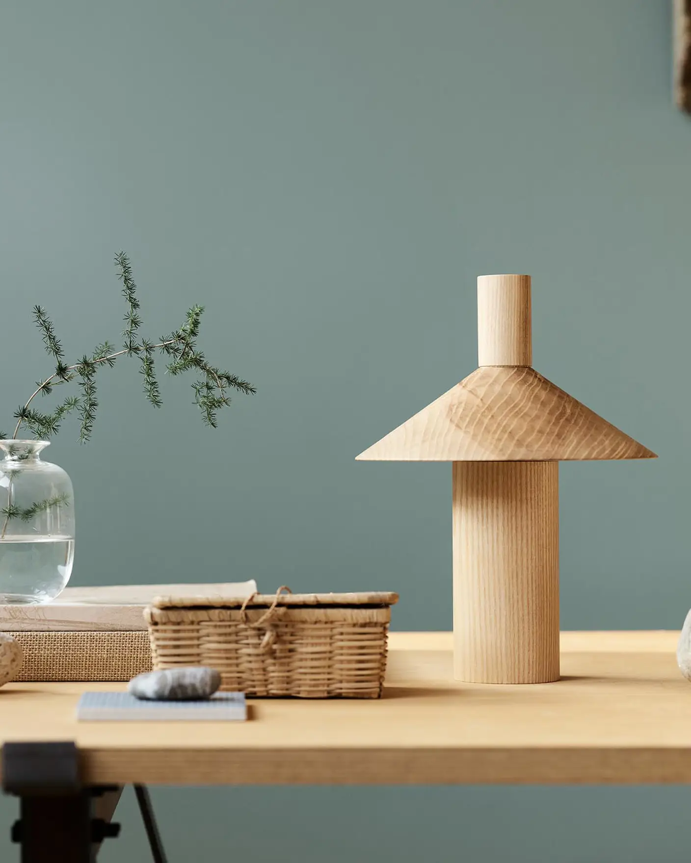 Minimalist decor with vase, books, and sculpture on a wooden table against a muted, bluish green background in the colour Jotun 6379 Cityscape.