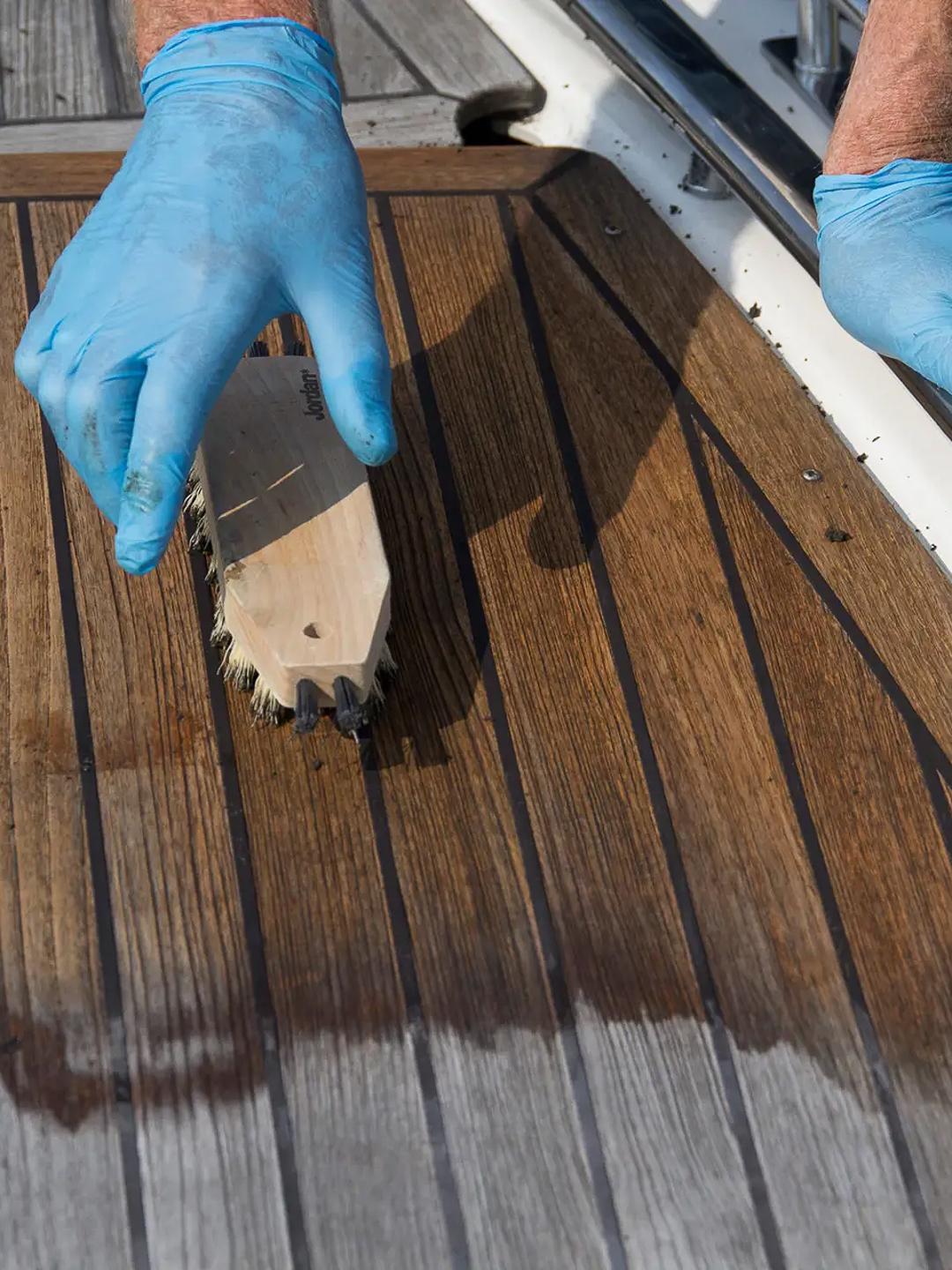 Vasking av teakdekk på båt med skrubb og hansker på