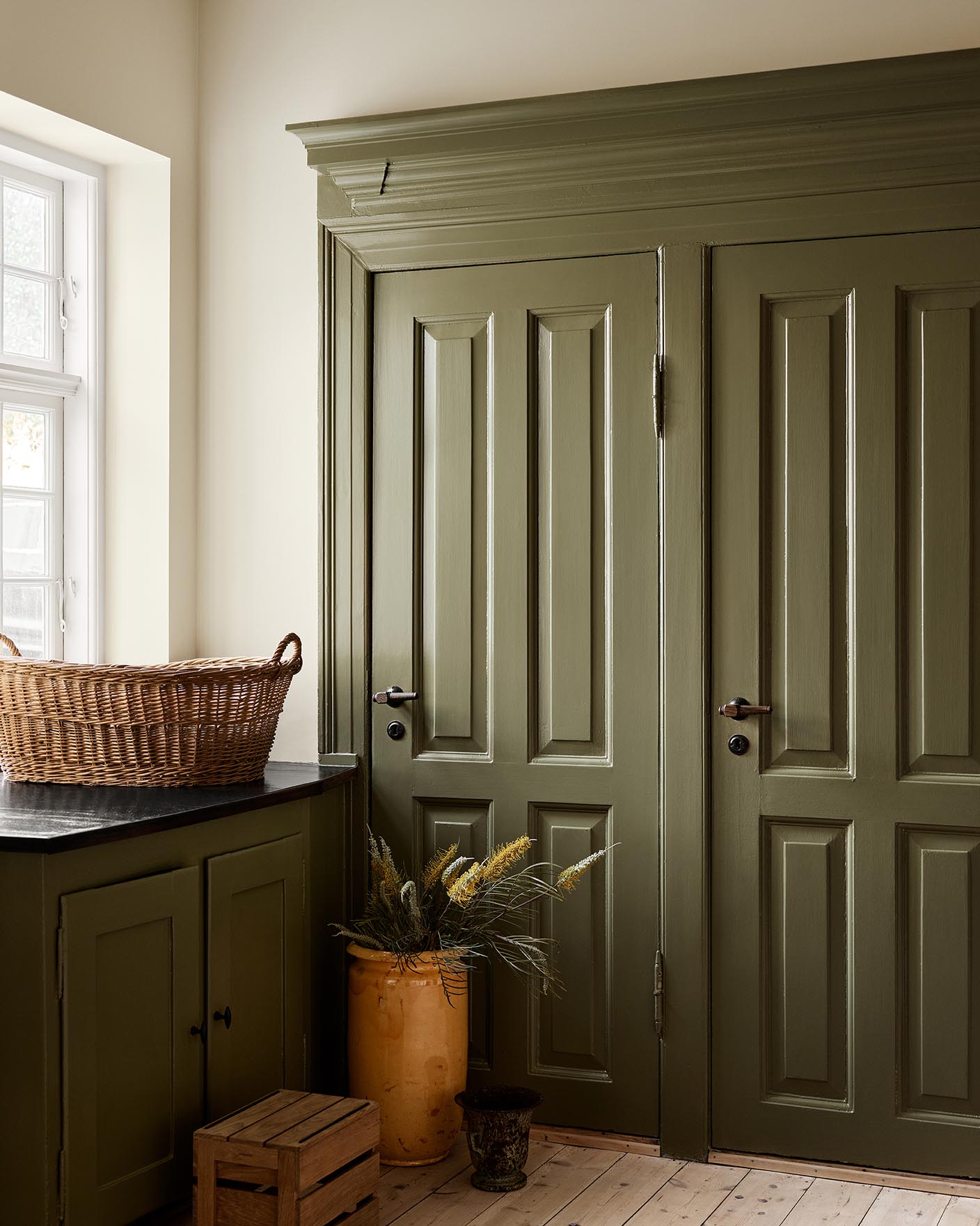 Kitchen with olive-green cabinets in the colour 8597 Seaweed Green against a muted yellow wall painted with 12079 Gleam from Jotun.