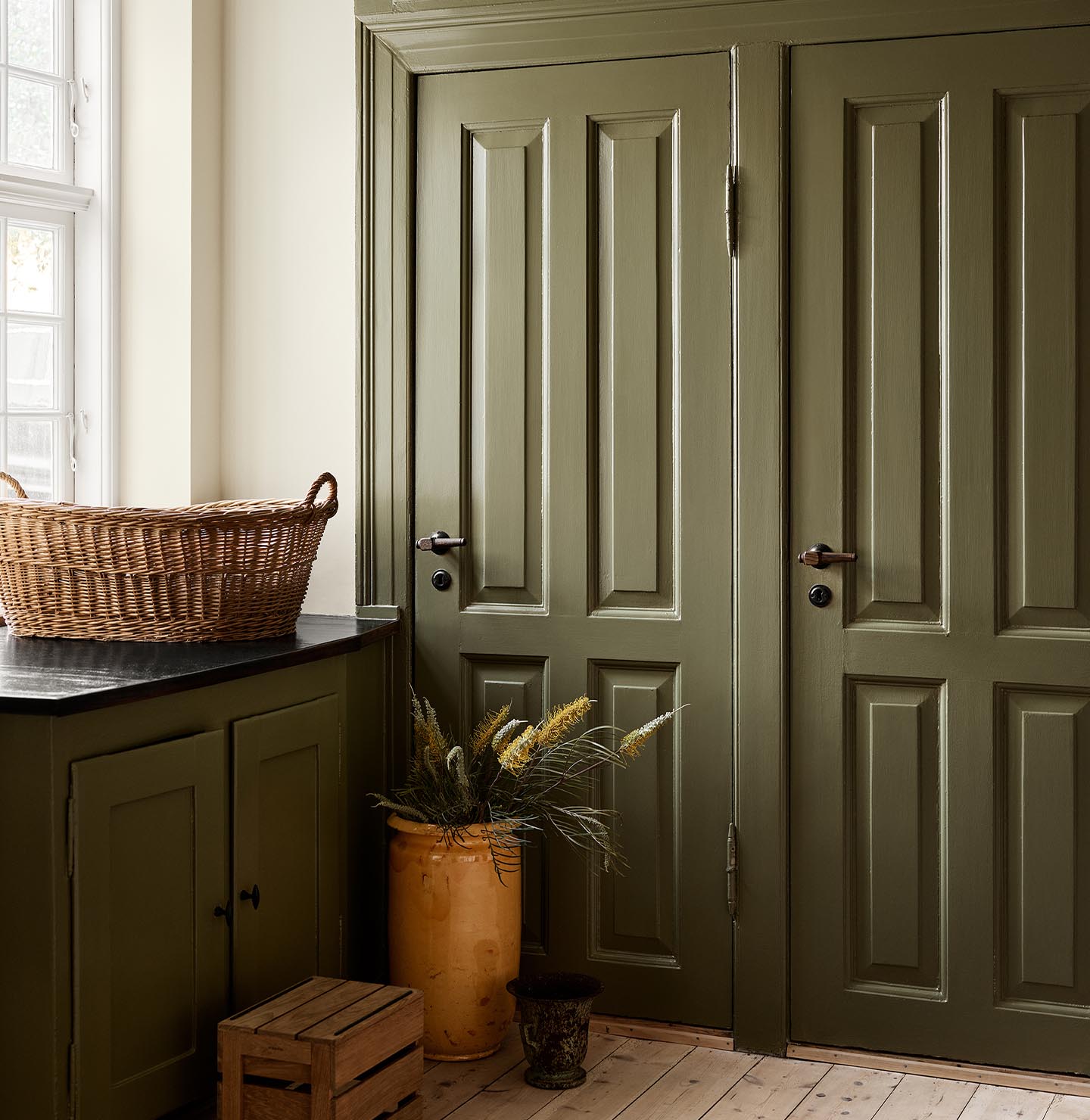 Kitchen with olive-green cabinets in the colour 8597 Seaweed Green against a muted yellow wall painted with 12079 Gleam from Jotun.