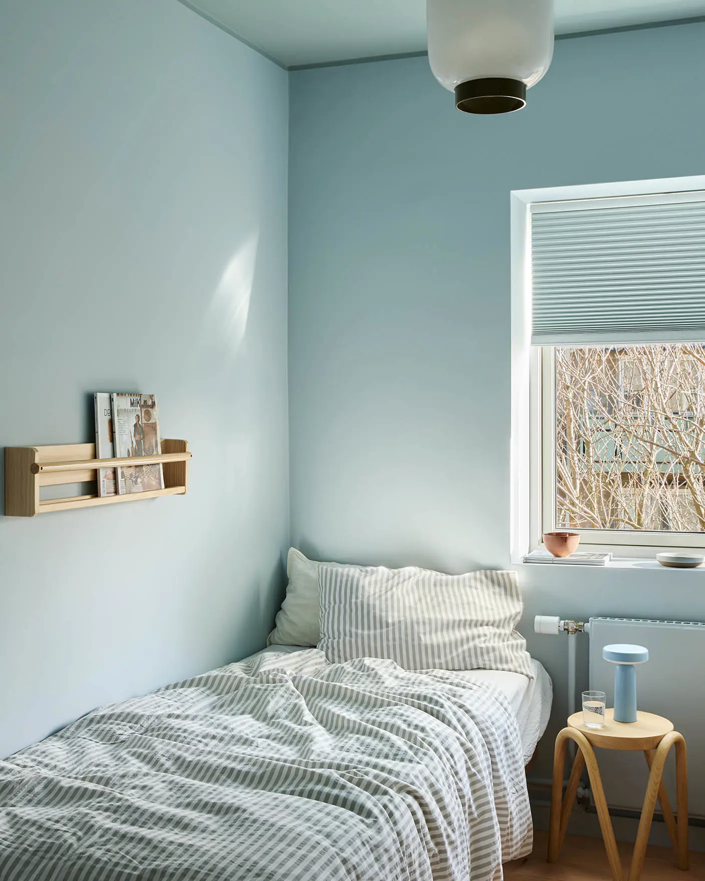 Bedroom painted in Jotun 6167 Spring Breeze with ceiling in 6236 Darjeeling; minimal décor with light wood stool and striped bedding.