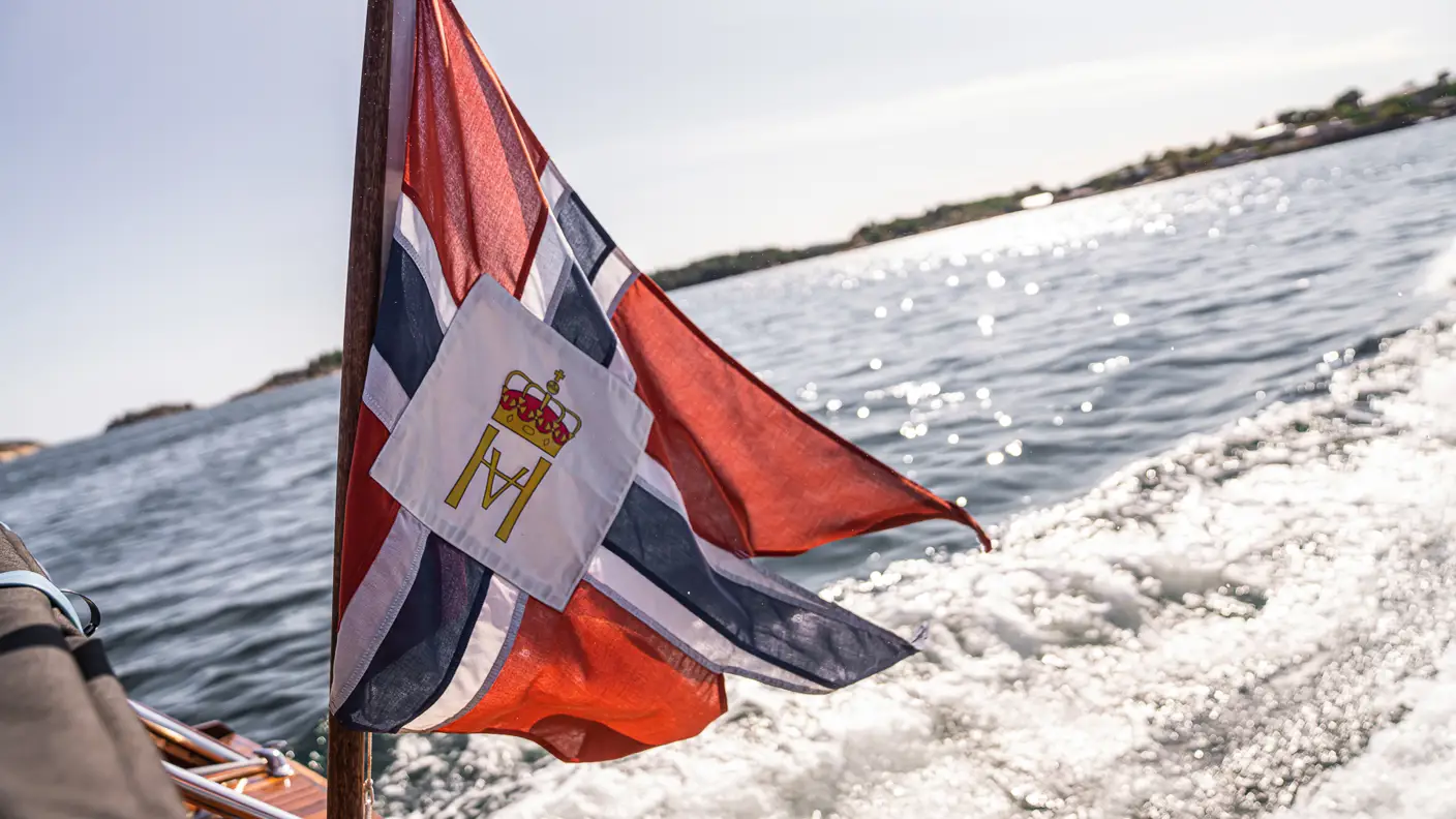 Flagg som vaier i vinden fra kjølvannet bak en båt i fart, i sol