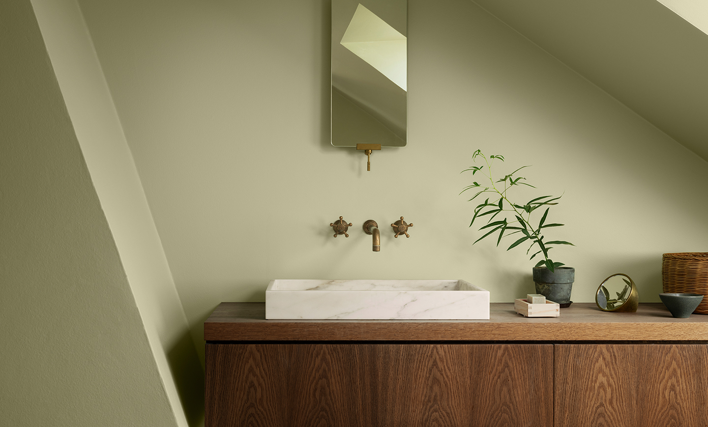 Moderne baderom malt med våtromsmalingen LADY Aqua i den lyst grønne fargen Jotun Sunny Green, med hvit marmorvask, veggmontert armatur, og trekabinett. Grønn plante og stilren innredning på benken. Veggene er malt i en lys olivengrønn farge