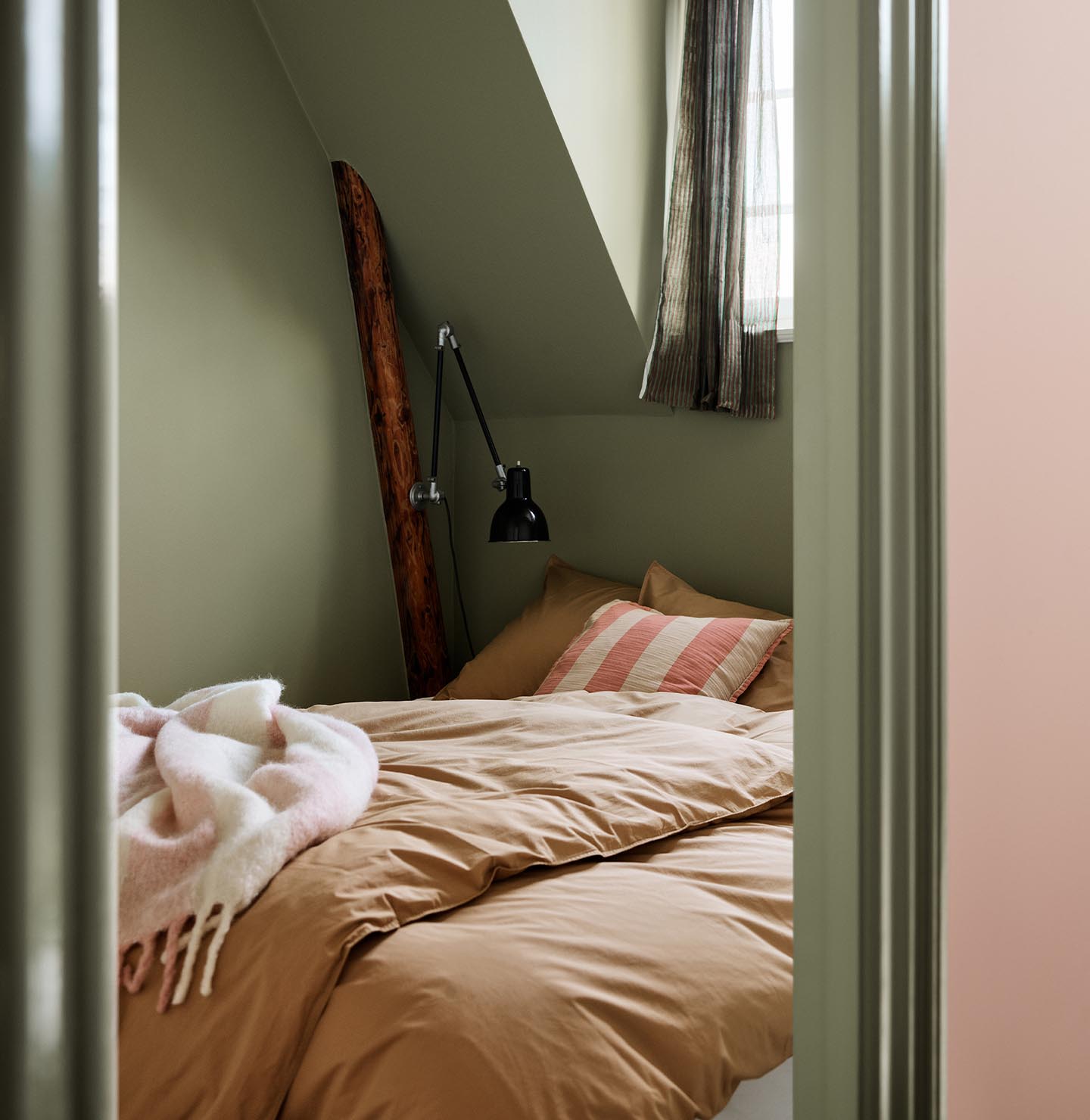 Bedroom with brown bedding and a pink-striped pillow against green painted walls and trims in the Jotun colour 8493 Green Tea.