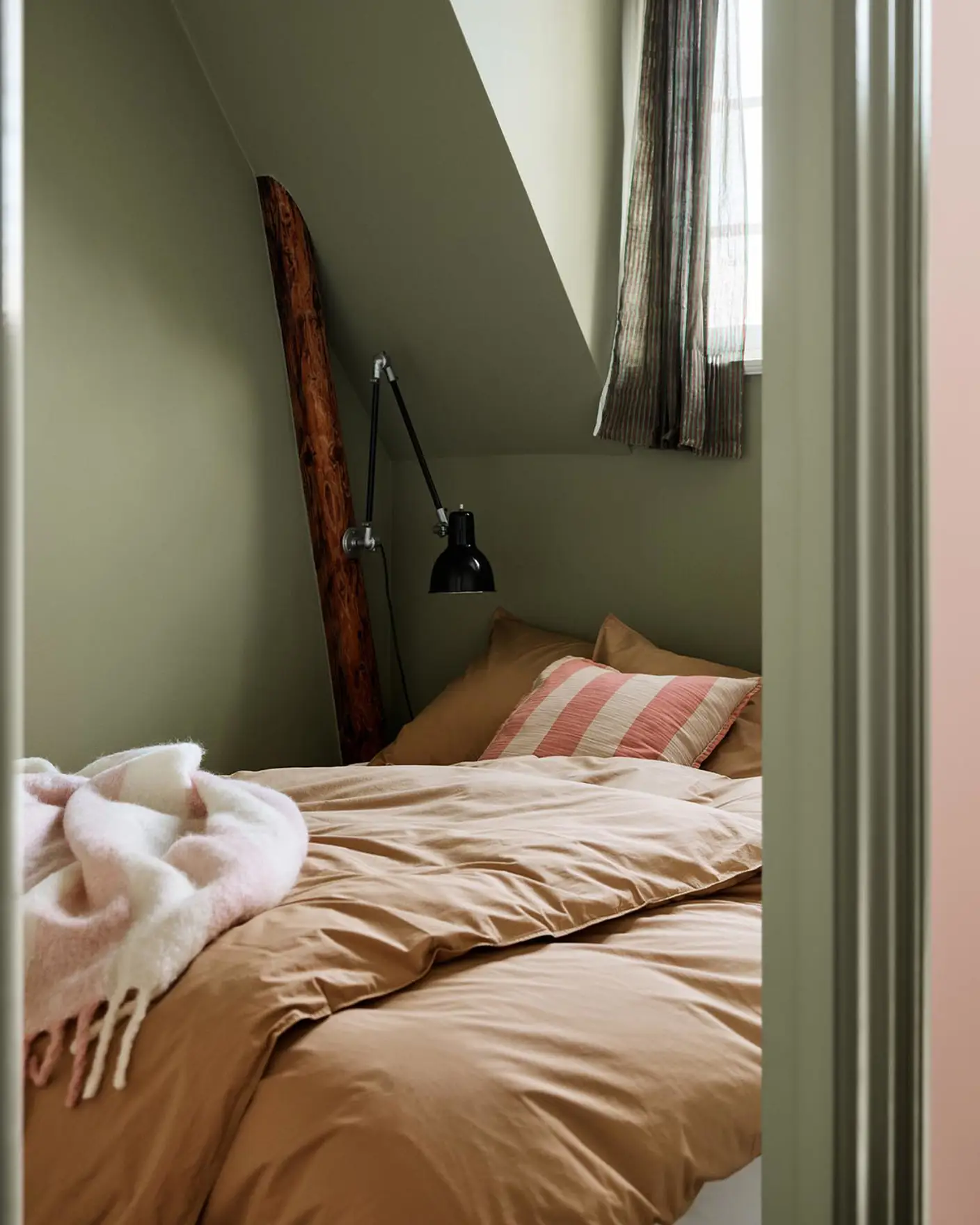 Bedroom with brown bedding and a pink-striped pillow against green painted walls and trims in the Jotun colour 8493 Green Tea.