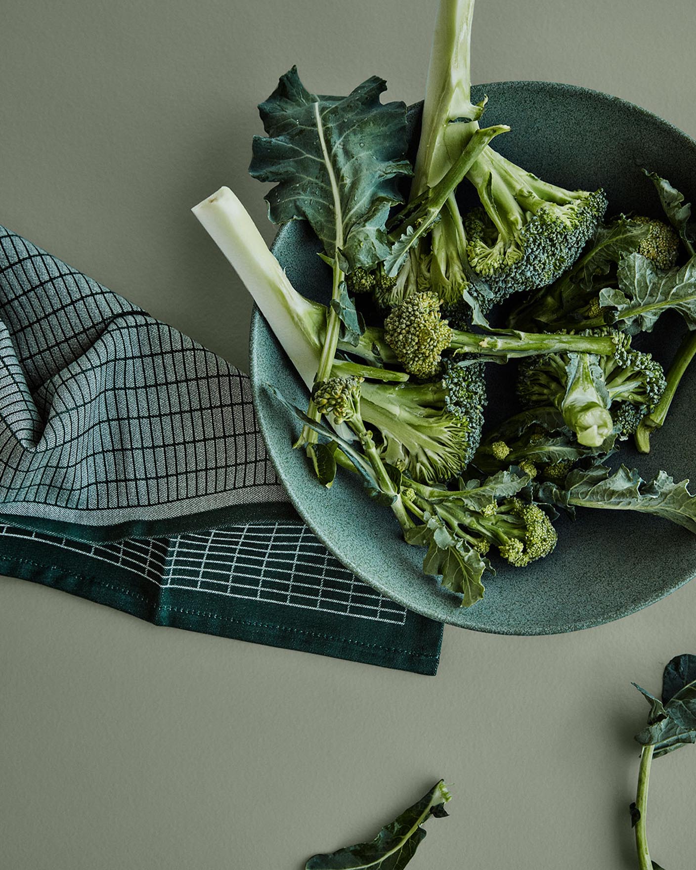 Fersk brokkoli i en grønn keramisk bolle står på en dempet grønn overflate malt med fargen 7628 Treasure fra Jotun, for en rolig, jordnær kjøkkenfølelse.