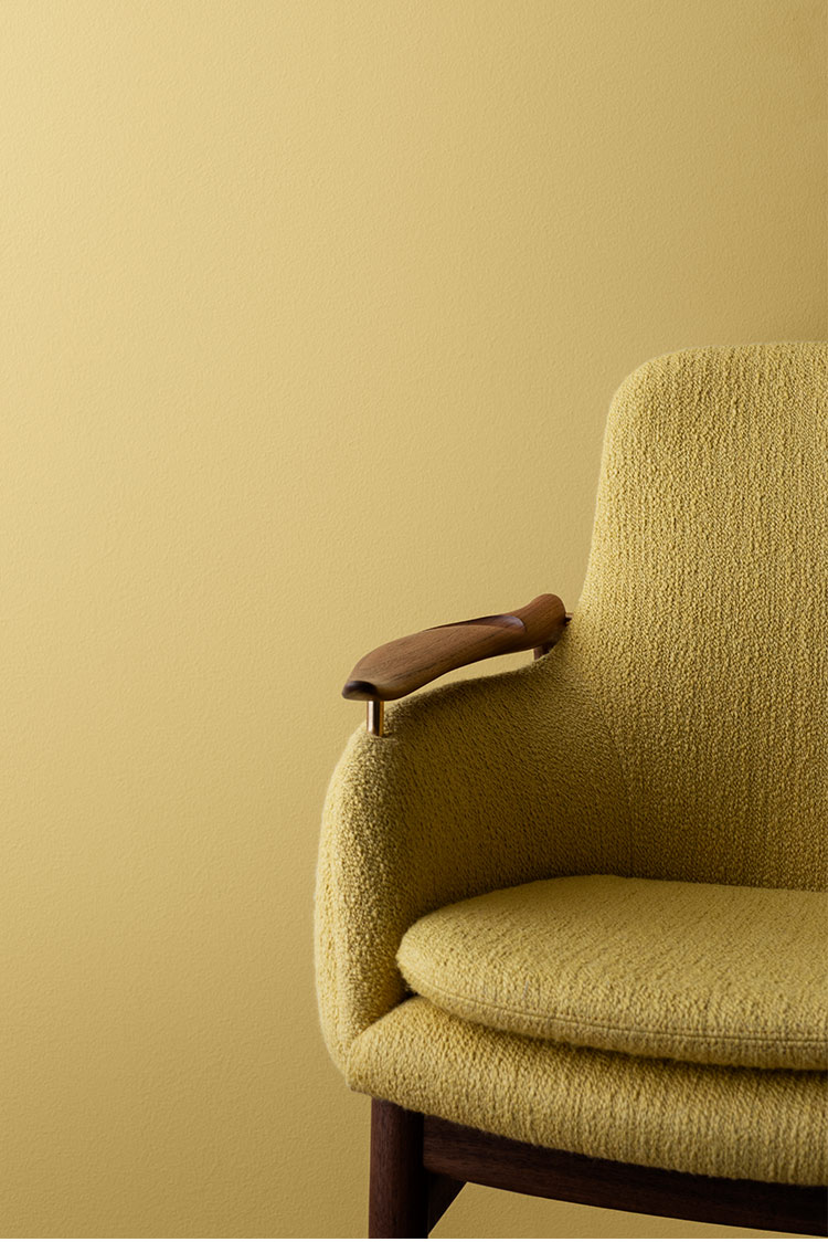 1950-talls gul lenestol med trearmstøtte mot en matchende gul vegg malt i Jotun 10235 Sommersol