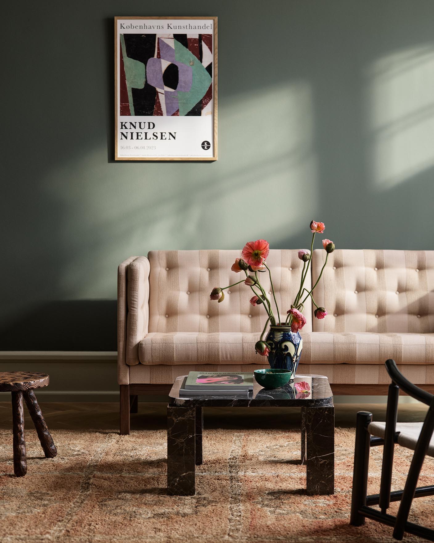 Living room with a sofa with sunlight streaming through a window. The background wall is painted with the dark, muted green colour 7613 Northern Mystic from Jotun.