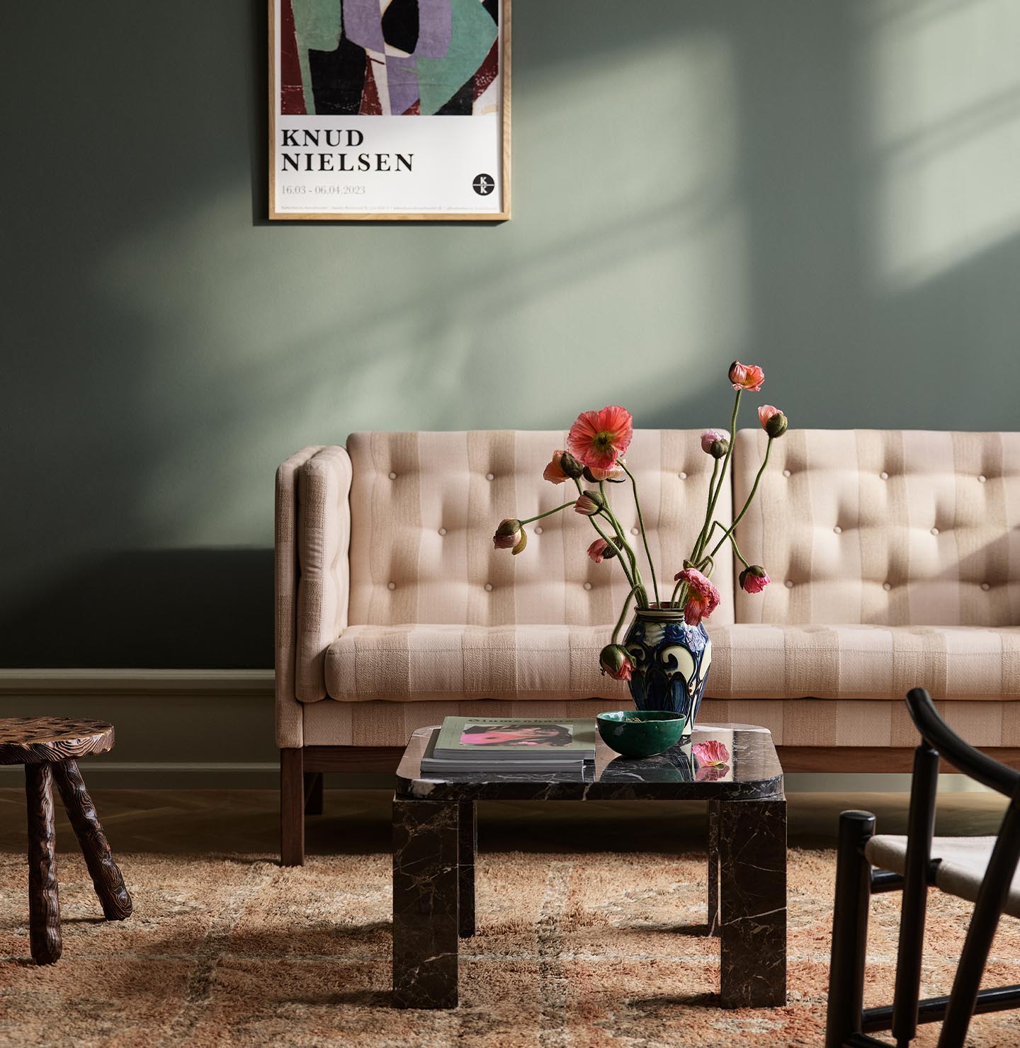 Living room with a sofa with sunlight streaming through a window. The background wall is painted with the dark, muted green colour 7613 Northern Mystic from Jotun.