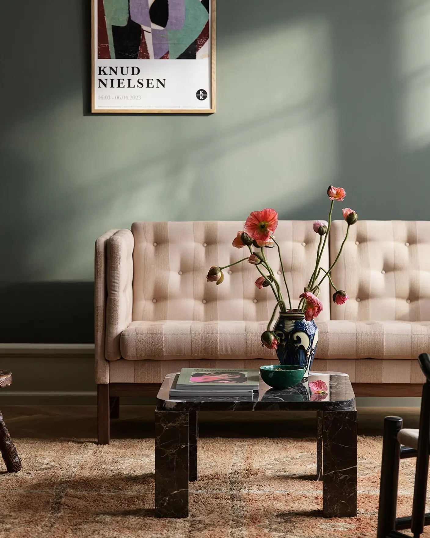 Living room with a sofa with sunlight streaming through a window. The background wall is painted with the dark, muted green colour 7613 Northern Mystic from Jotun.