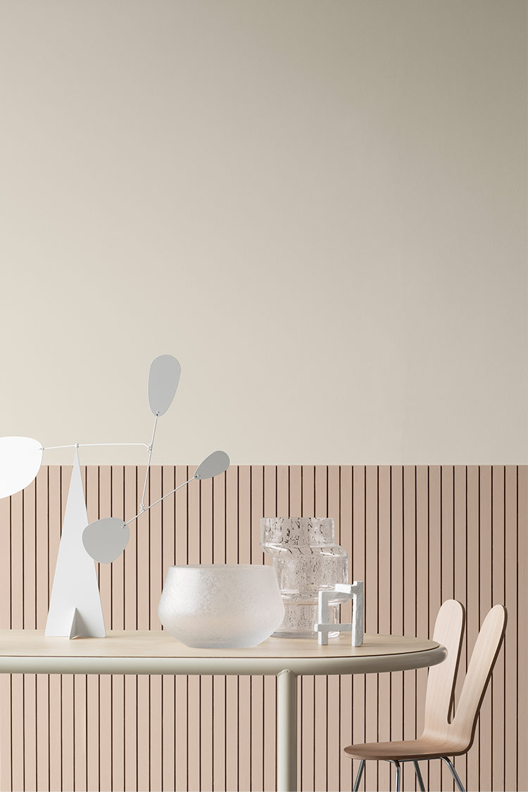 Moderne interiørdesign med et beige rundt bord, en minimalistisk skulptur, transparente glassvaser og en unik trestol mot en vertikalt linjet vegg