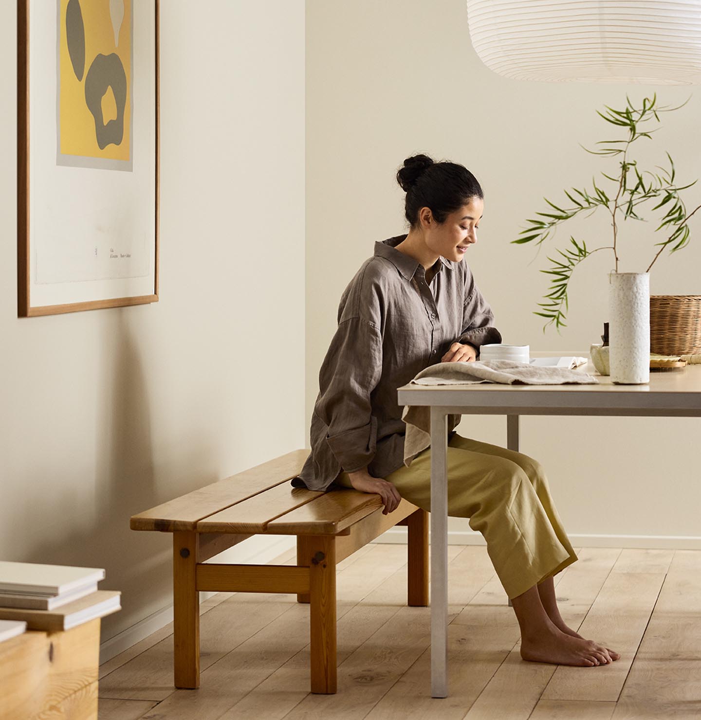 Woman sitting on a wooden bench by a desk with beige walls painted in the colour Jotun 12308 Unbleached.