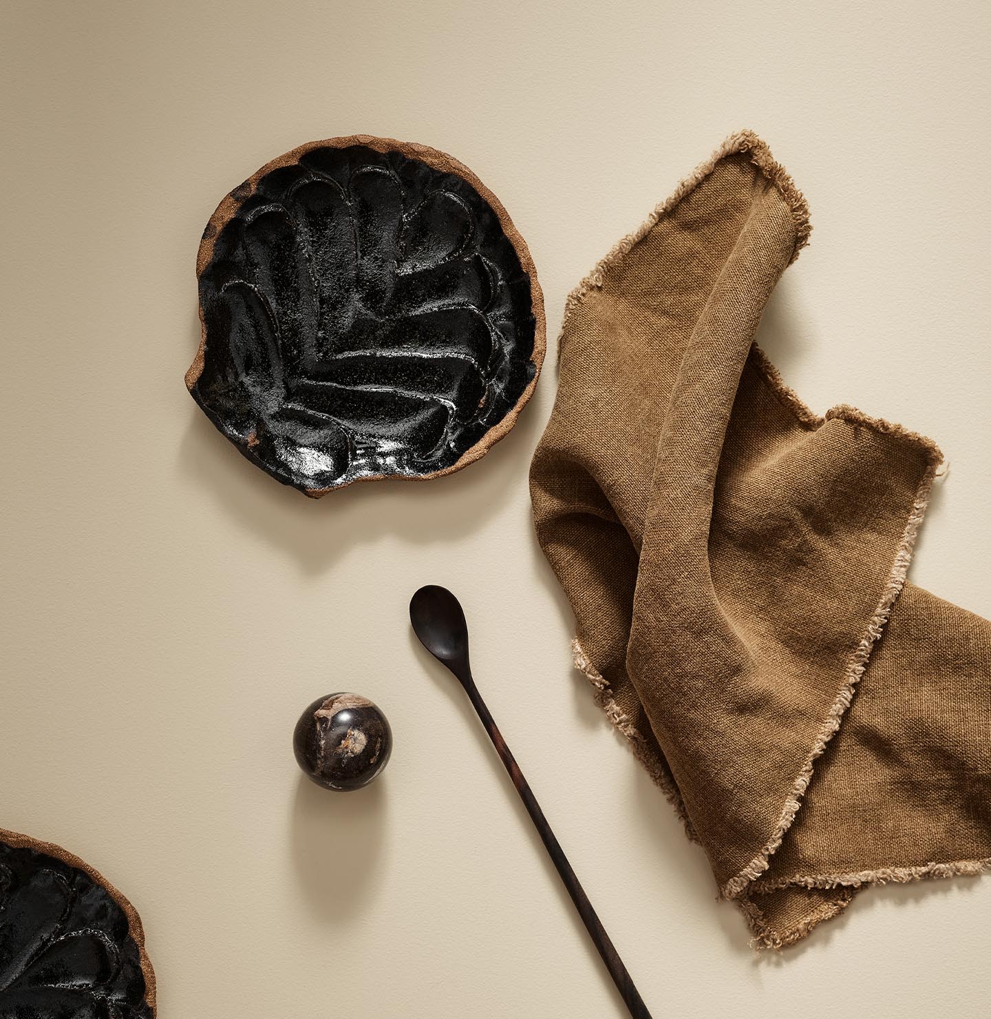 Black ceramic plate with a spoon and brown cloth on a beige surface in the colour 1303 Observe from Jotun.