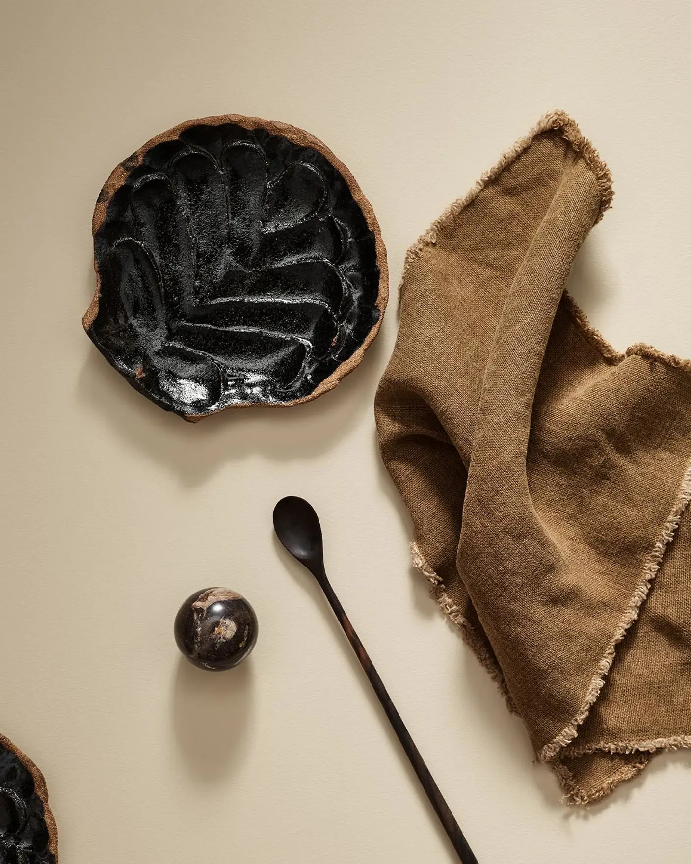 Black ceramic plate with a spoon and brown cloth on a beige surface in the colour 1303 Observe from Jotun.