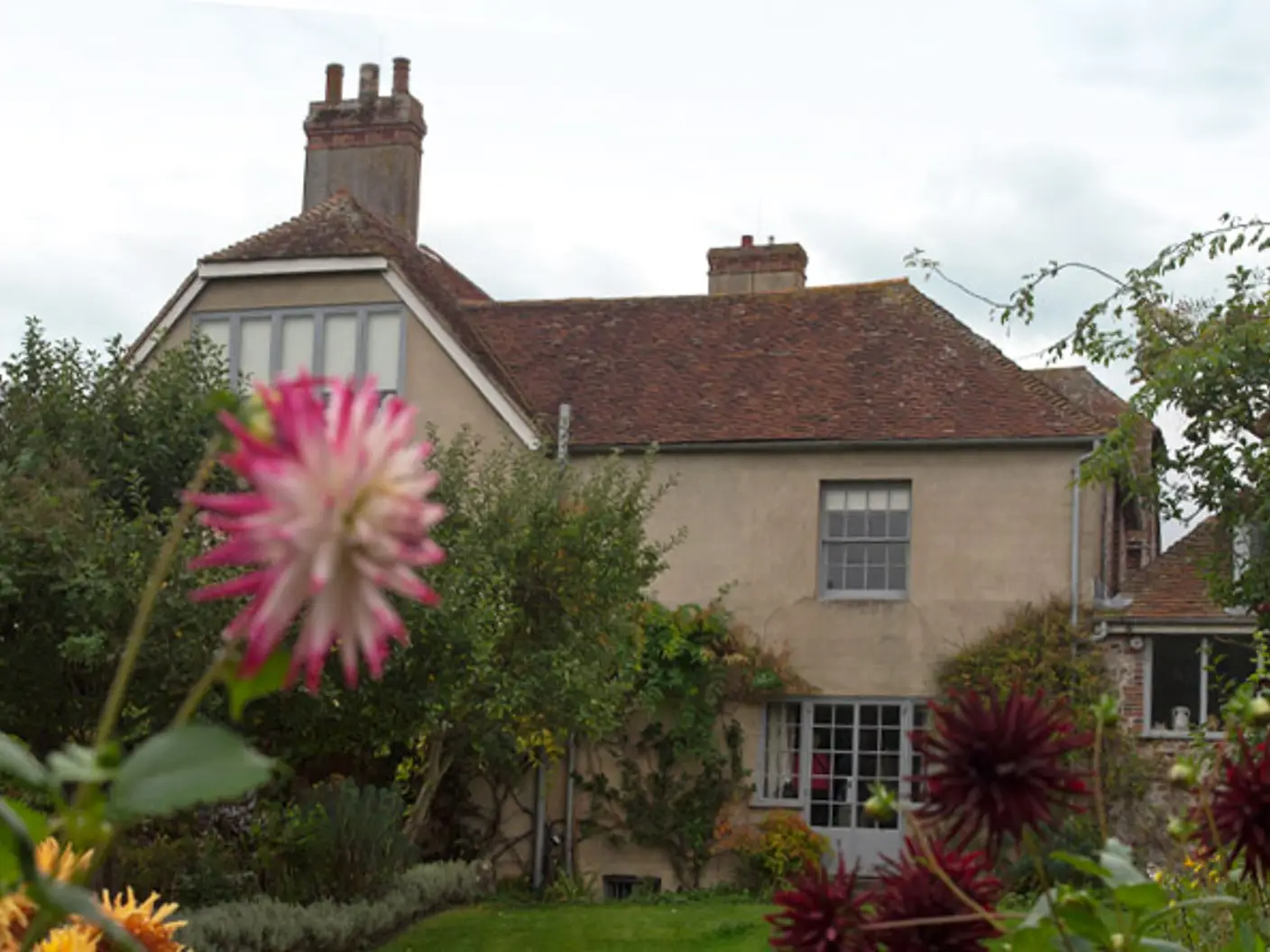 Historisk engelsk landsted med rød takstein, omgitt av en frodig hage og blomstrende blomster, under en skyet himmel