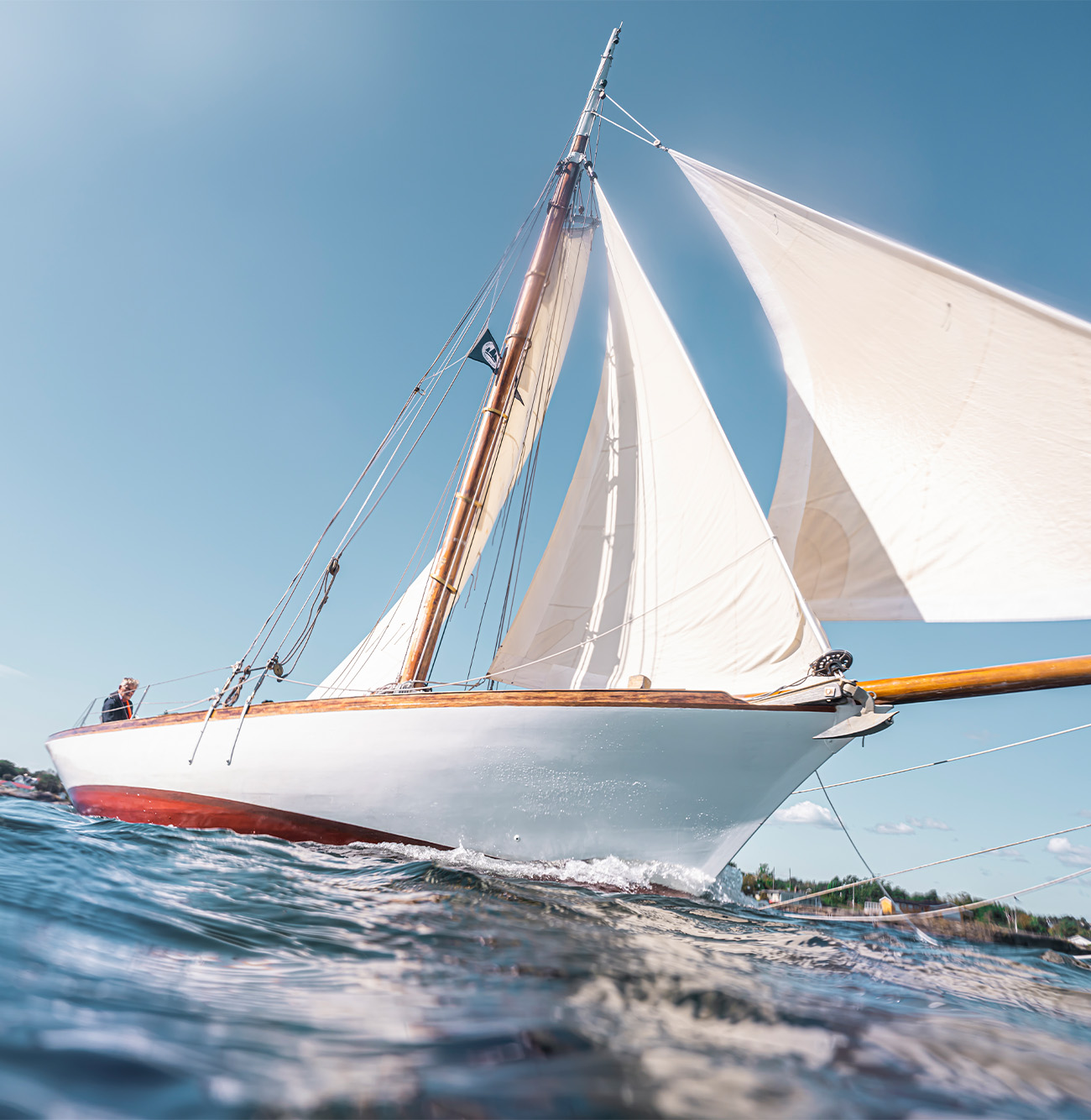 Seilbåt med hvite seil som skjærer gjennom vannet på en klar sommerdag.