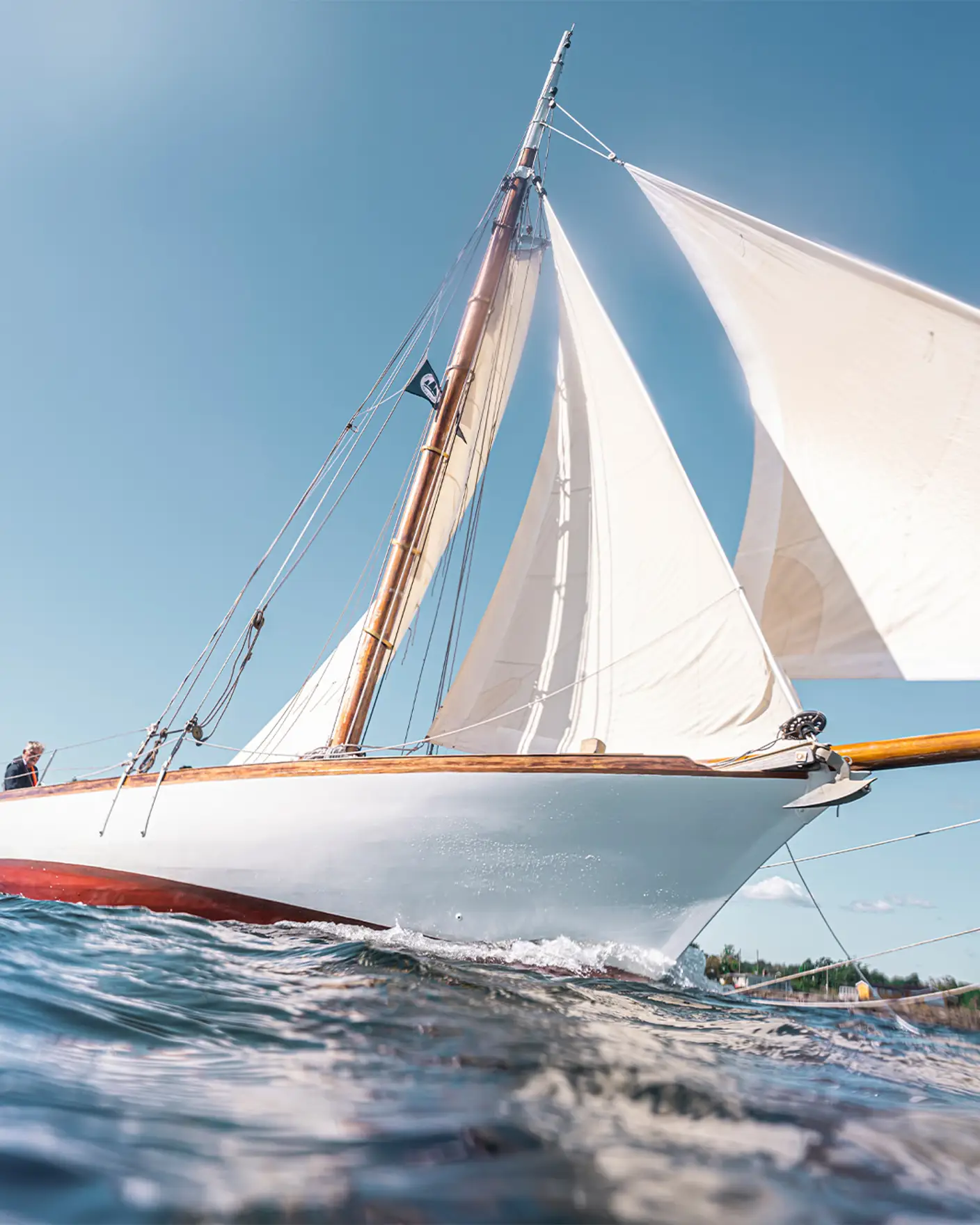 Seilbåt med hvite seil som skjærer gjennom vannet på en klar sommerdag.