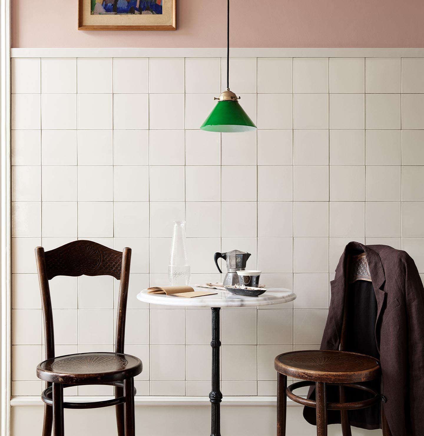 A table and wooden chairs in front of a tiled wall. The upper wall is painted in the soft pink colour Jotun 20362 Pink Ambience. 