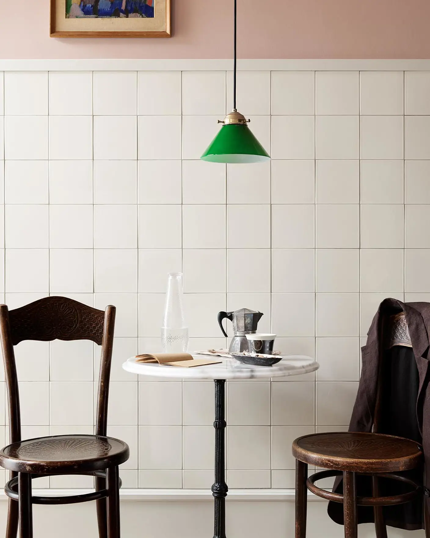 A table and wooden chairs in front of a tiled wall. The upper wall is painted in the soft pink colour Jotun 20362 Pink Ambience.