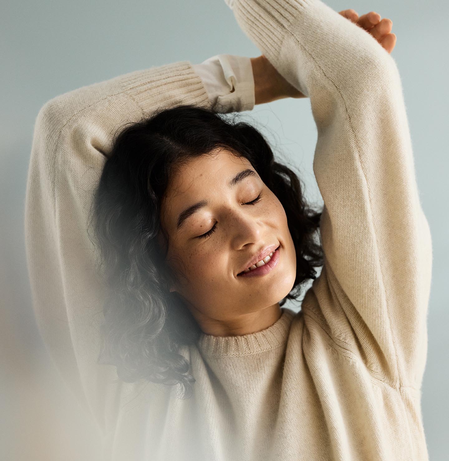 Woman with curly hair with arms raised above the head, in front of a muted blue background painted with the colour 6378 Iconic from Jotun.