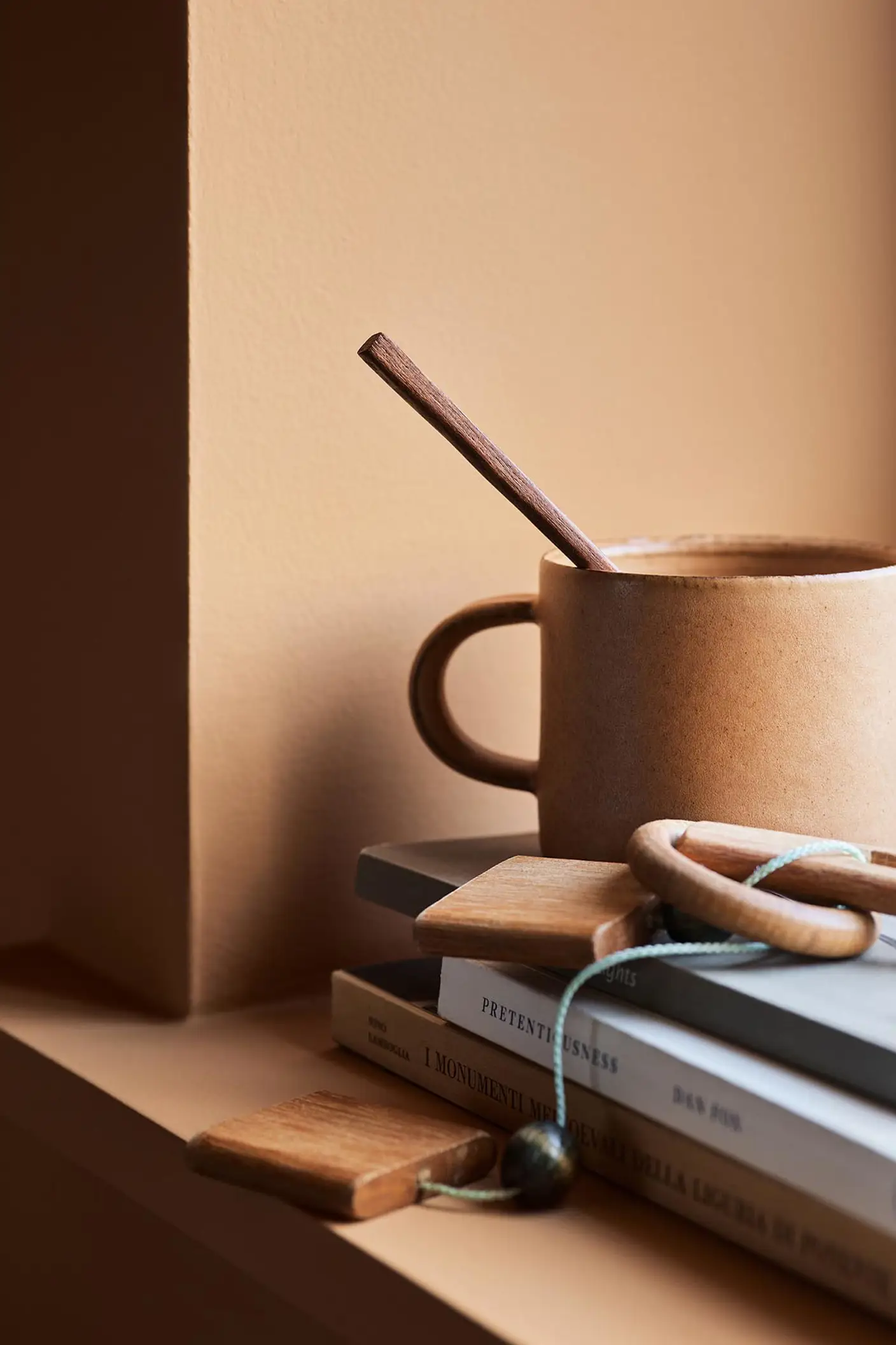 Ceramic mug with a wooden stirrer on stacked books against a ochre wall painted with the Jotun colour 11220 Ochre Clay.