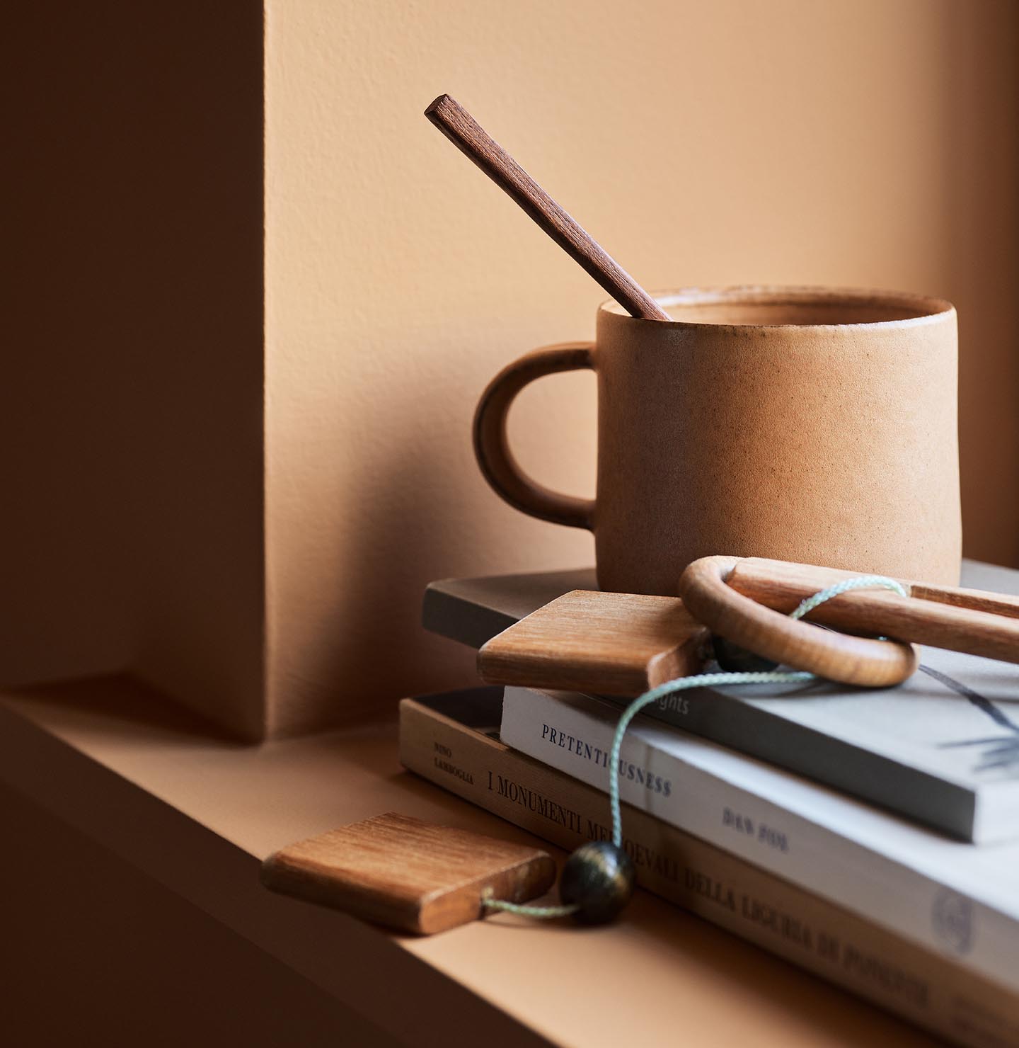 Ceramic mug with a wooden stirrer on stacked books against a ochre wall painted with the Jotun colour 11220 Ochre Clay.