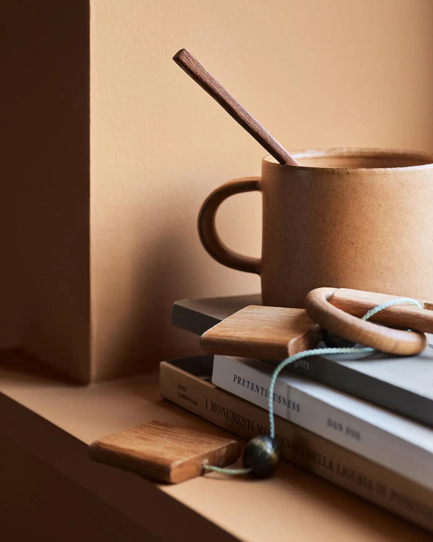 Ceramic mug with a wooden stirrer on stacked books against a ochre wall painted with the Jotun colour 11220 Ochre Clay.