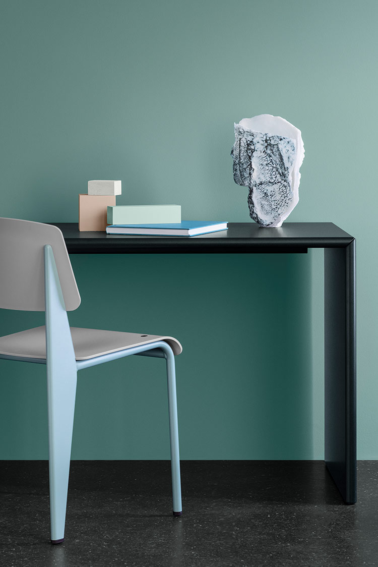 Moderne minimalistisk interiør med svart bord, lyseblå stol og teksturert skulptur mot turkis vegg malt i Jotun 6084 Sea Emerald