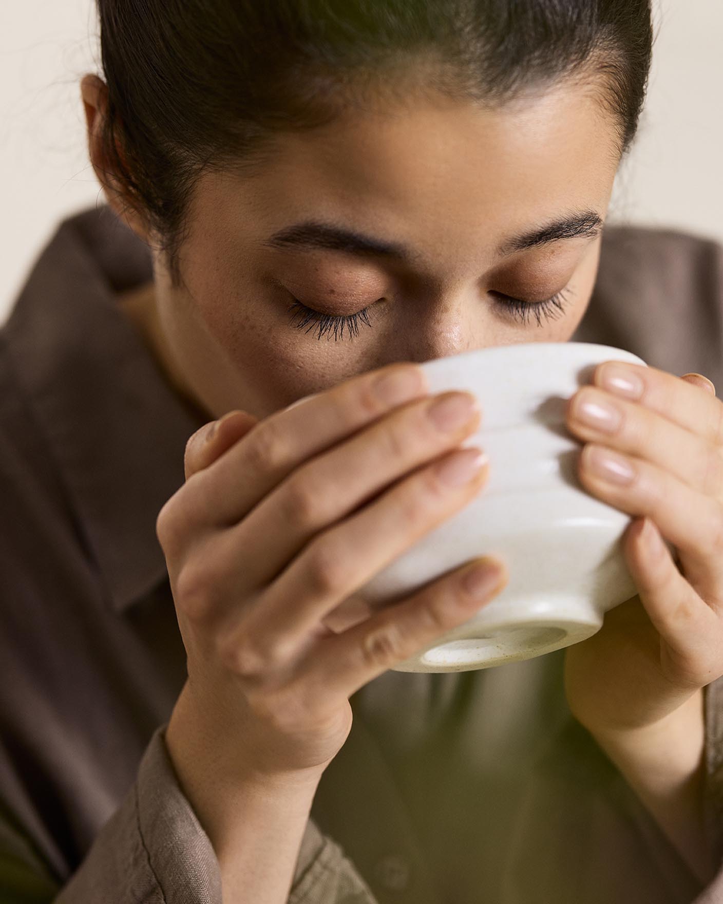 Woman drinking from a cup with a beige background in the colour Jotun 12308 Unbleached.