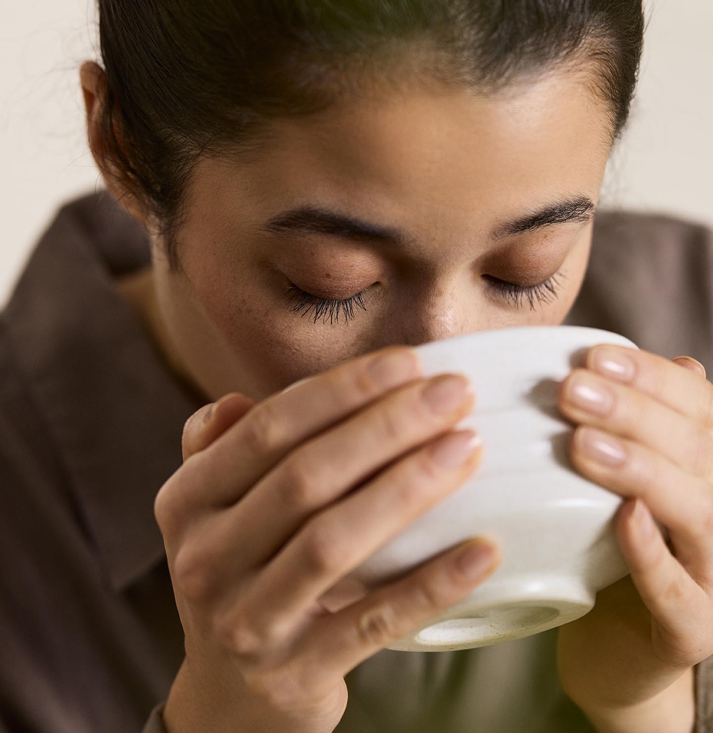 Woman drinking from a cup with a beige background in the colour Jotun 12308 Unbleached.
