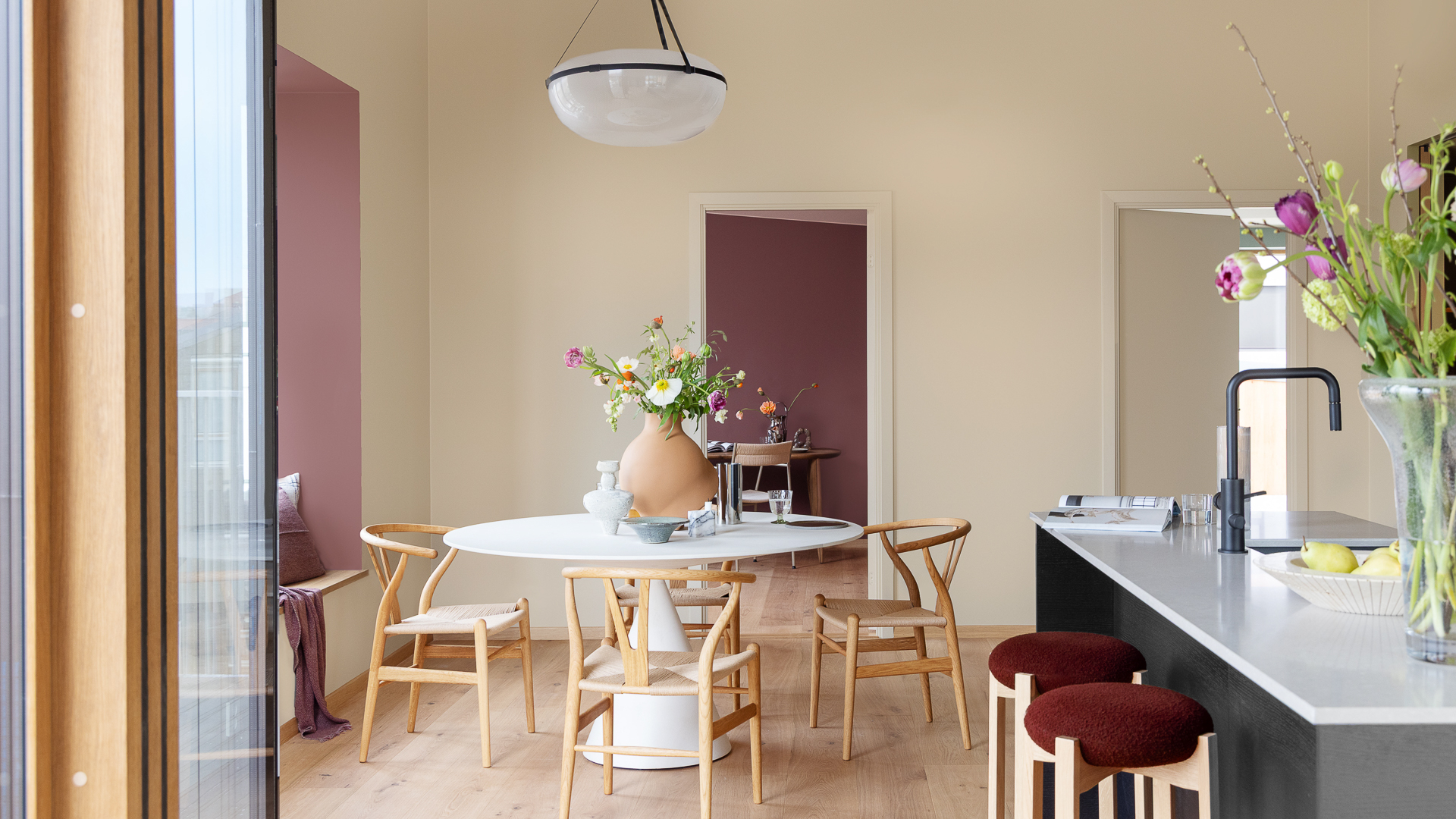 Spisestue med moderne møbler og kjøkkenøy, vegger i myk, gyllen beige malt i JOTUN 1303 Observe, karnapp og rom på innsiden malt i rødt i fargen JOTUN 2951 Sophisticated Red