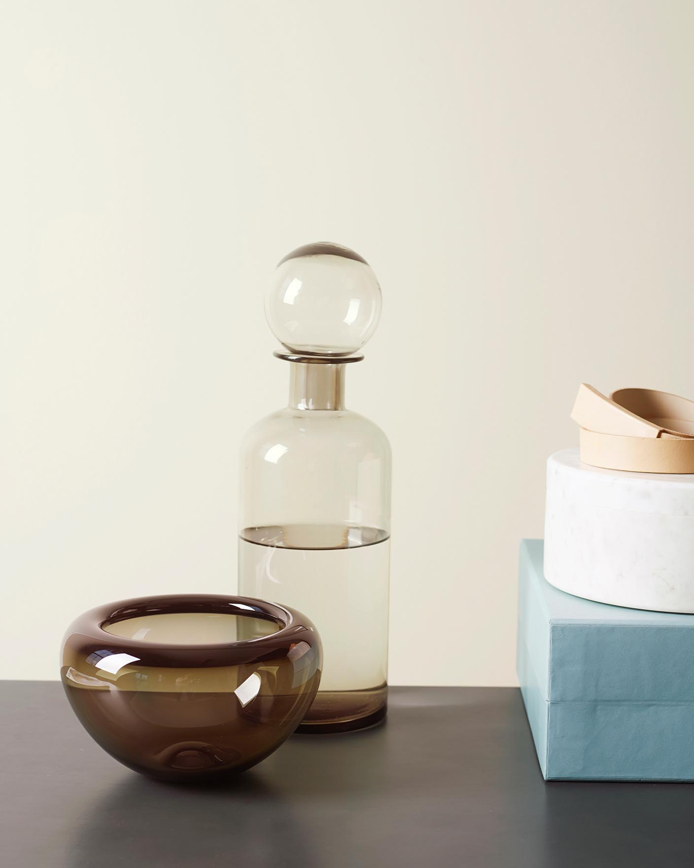 Estilo minimalista con paredes grisáceas suaves pintadas con Jotun 1928 Summer Snow y piezas escultóricas de vidrio y cerámica en tonos neutros cálidos y fríos.