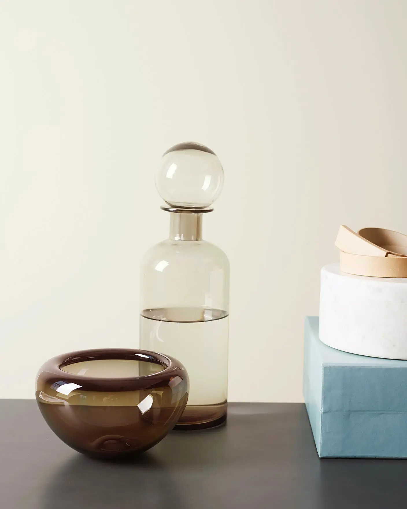 Estilo minimalista con paredes grisáceas suaves pintadas con Jotun 1928 Summer Snow y piezas escultóricas de vidrio y cerámica en tonos neutros cálidos y fríos.