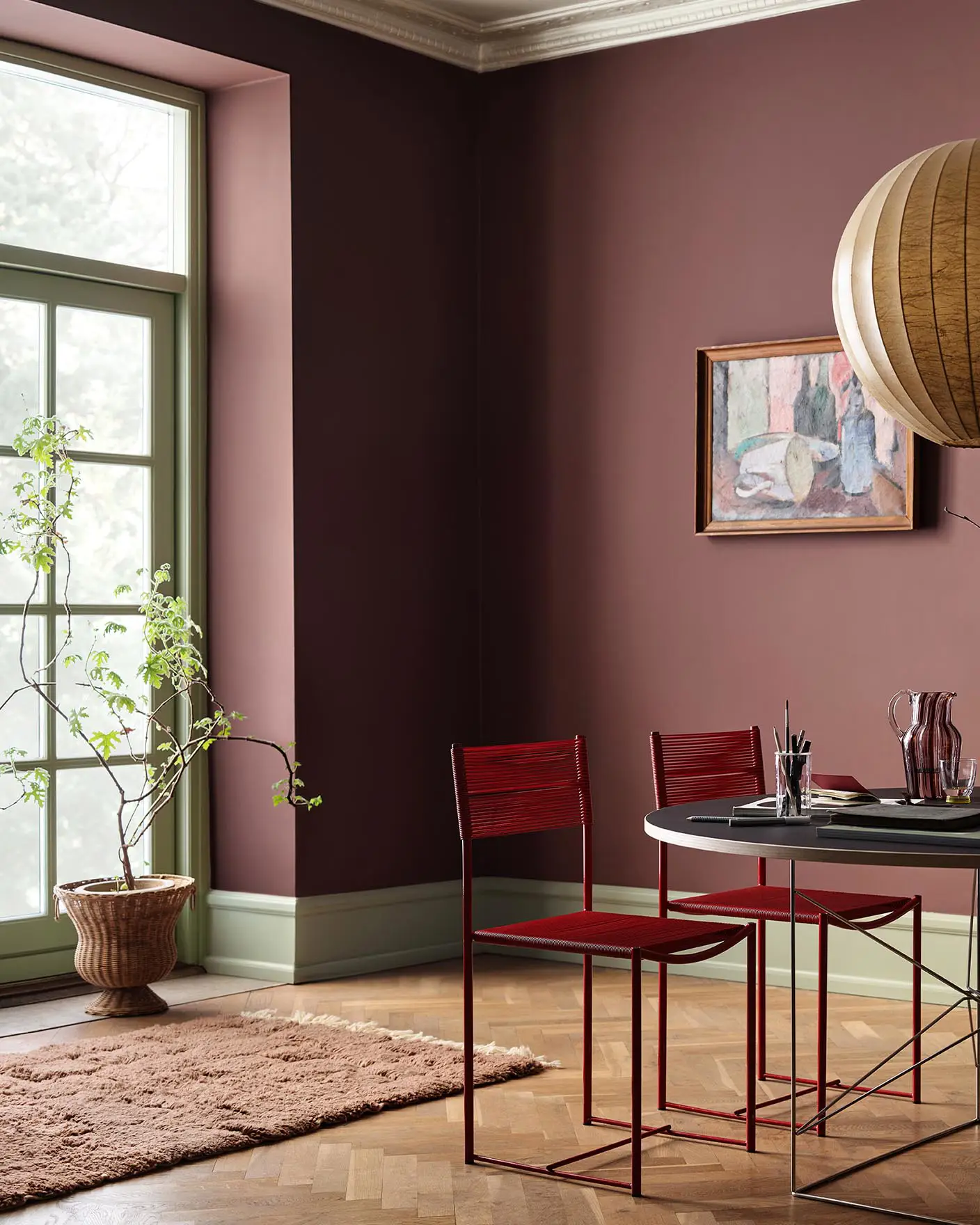 Dining area with chairs and a round table against deep red walls painted in 2951 Sophisticated Red from Jotun and green trims in the colour 8493 Green Tea.