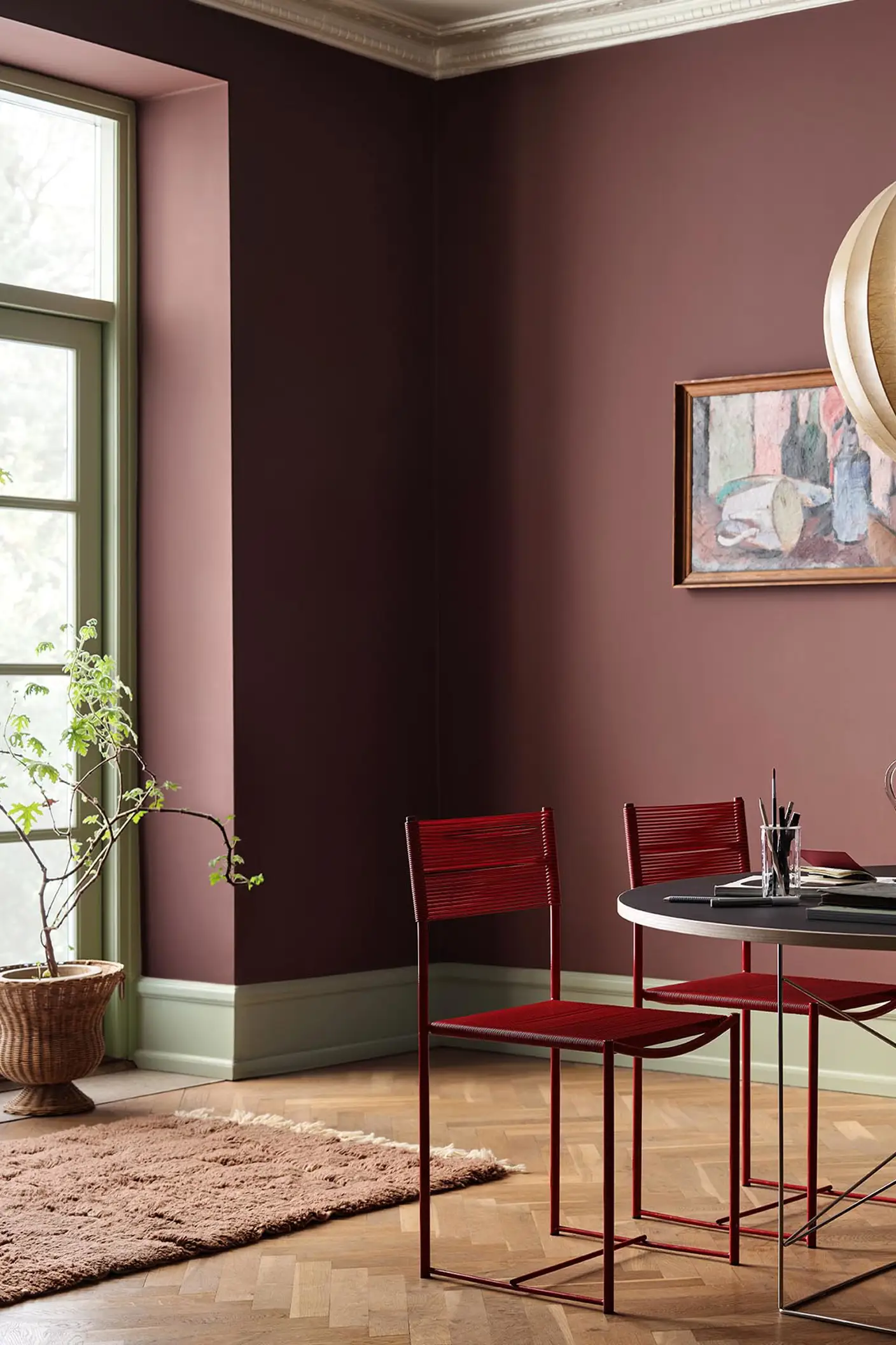 Dining area with chairs and a round table against deep red walls painted in 2951 Sophisticated Red from Jotun and green trims in the colour 8493 Green Tea.