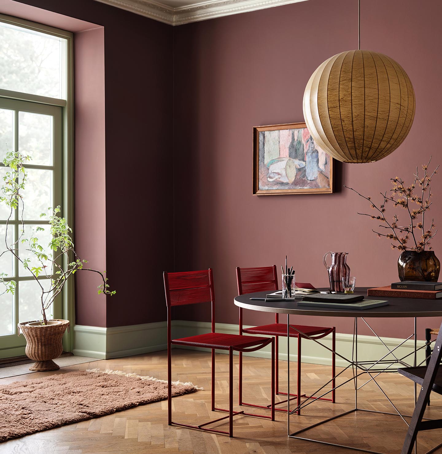 Dining area with chairs and a round table against deep red walls painted in 2951 Sophisticated Red from Jotun and green trims in the colour 8493 Green Tea.