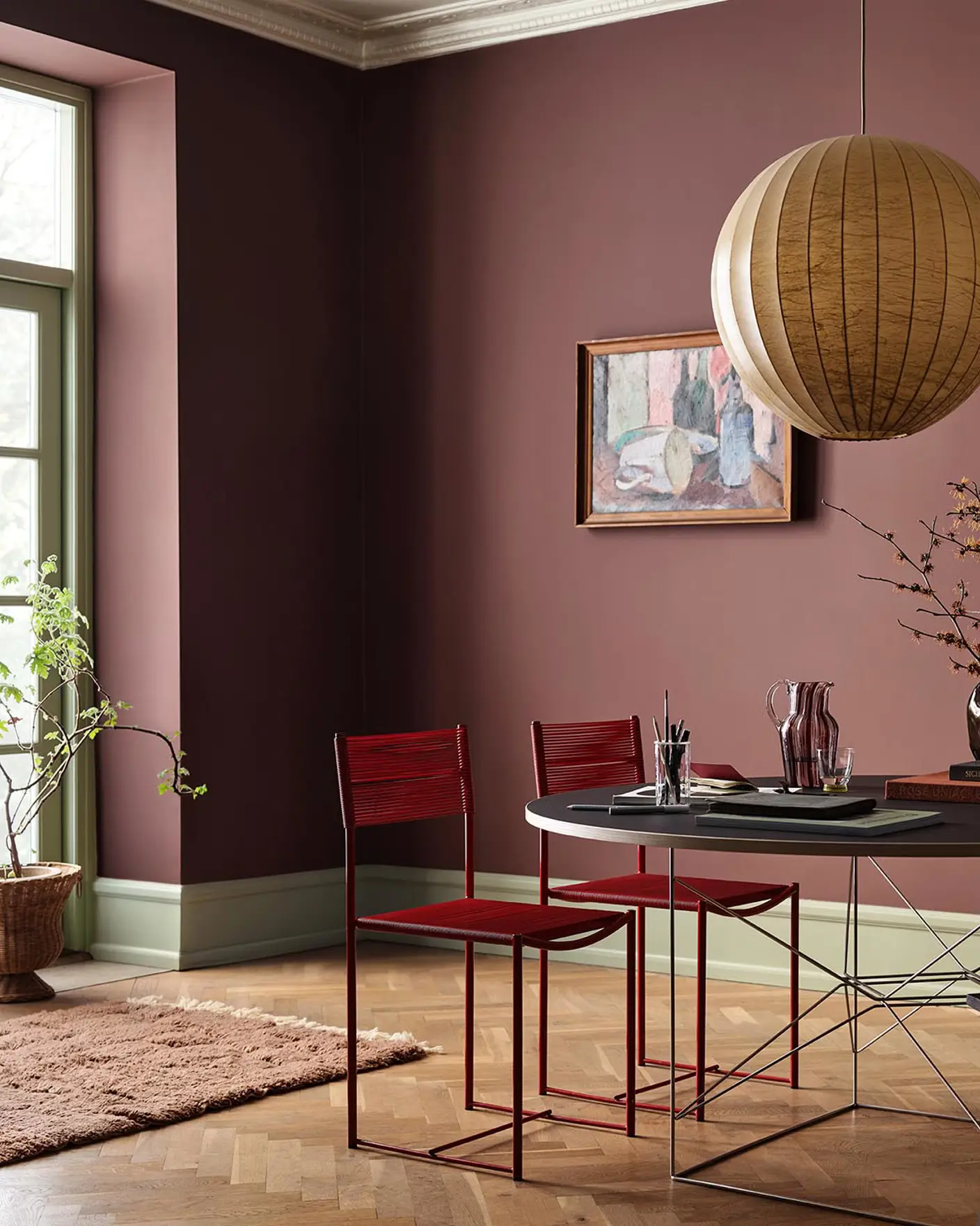 Dining area with chairs and a round table against deep red walls painted in 2951 Sophisticated Red from Jotun and green trims in the colour 8493 Green Tea.