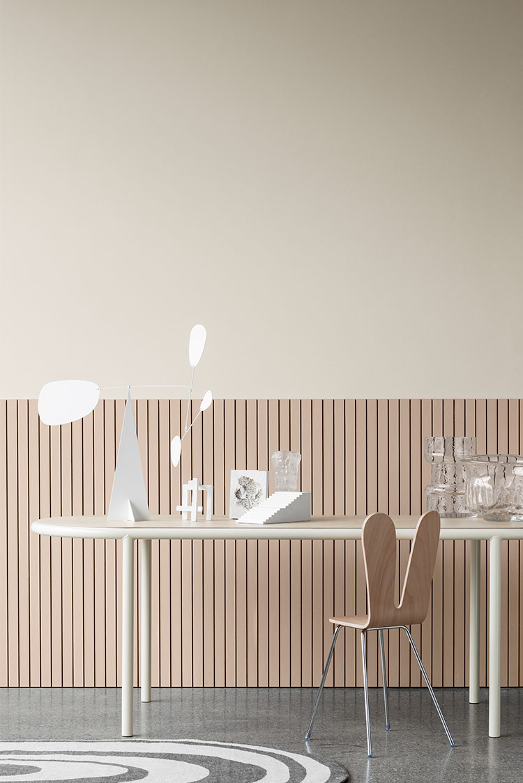 Moderne minimalistisk rom en rosa trepanelvegg malt i Jotun 20185 Friendly Pink og en slettvegg over malt beige i Jotun 12812 Gentle Whisper, med et hvitt ovalt bord dekorert med moderne skulpturer og glassgjenstander. En trestol med metallben er plassert ved siden av bordet, satt på et grått, teksturert gulv