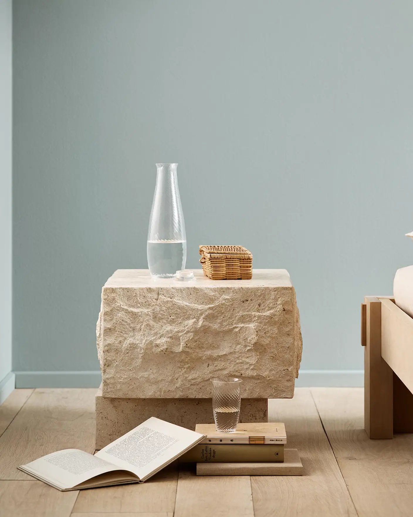 Minimalist bedroom with a stone bedside table and books on a wooden floor against a muted blue wall painted with 6378 Iconic from Jotun.