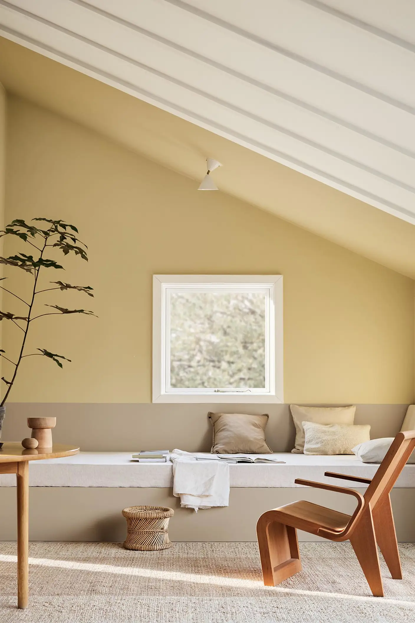 A daybed, wodden chair and a potted plant against muted, greenish yellow walls painted in the colour 1965 Ginger Tea from Jotun. Daybed painted in the colour 12300 Hazelnut Beige.