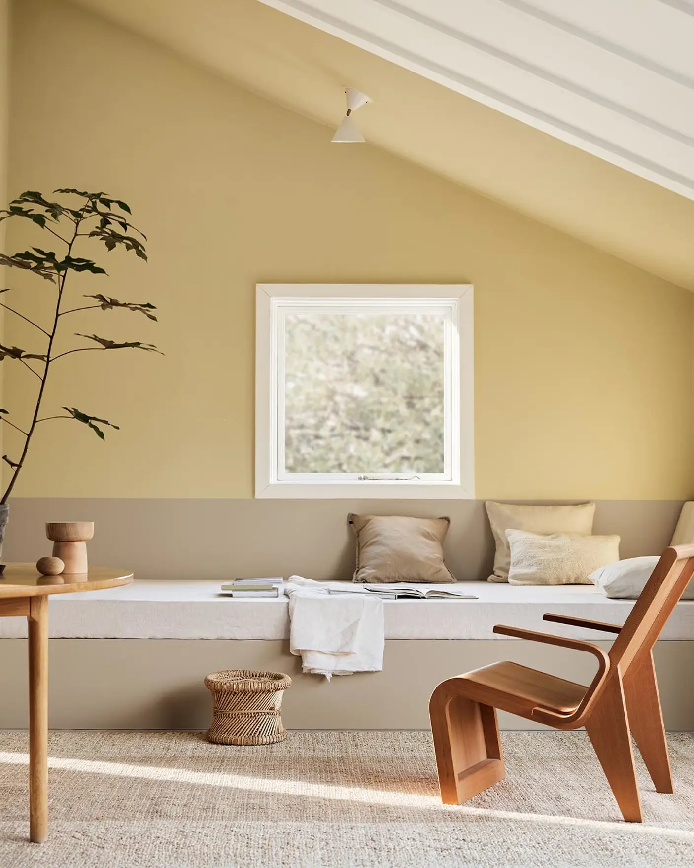 A daybed, wodden chair and a potted plant against muted, greenish yellow walls painted in the colour 1965 Ginger Tea from Jotun. Daybed painted in the colour 12300 Hazelnut Beige.