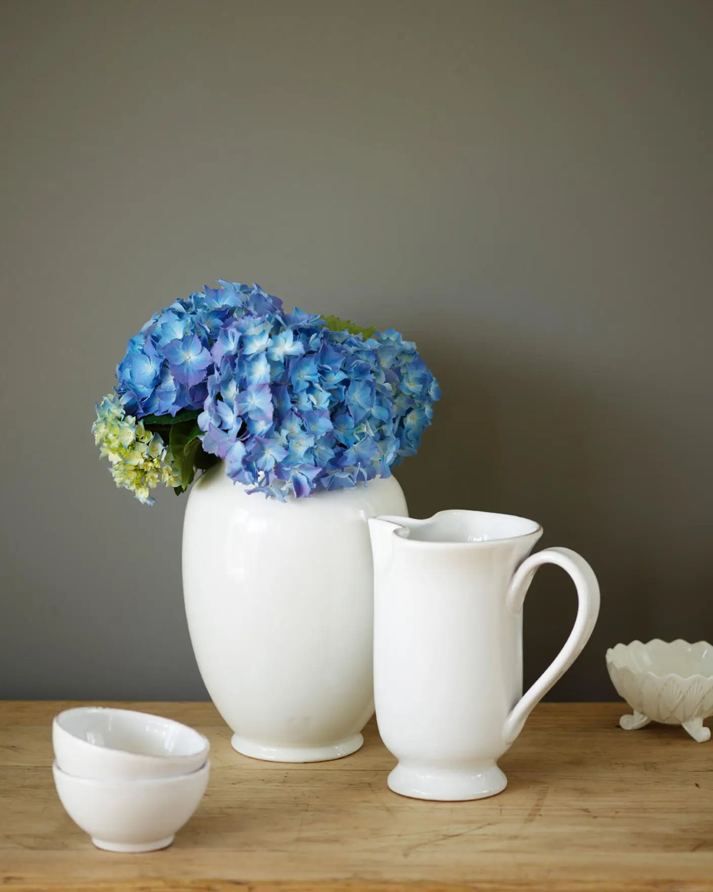 Cerámicas blancas y flores azul brillante frente a una pared pintada con Jotun 1462 Evening Sky, un color gris dorado. La madera natural aporta calidez y mantiene el conjunto tranquilo y equilibrado.